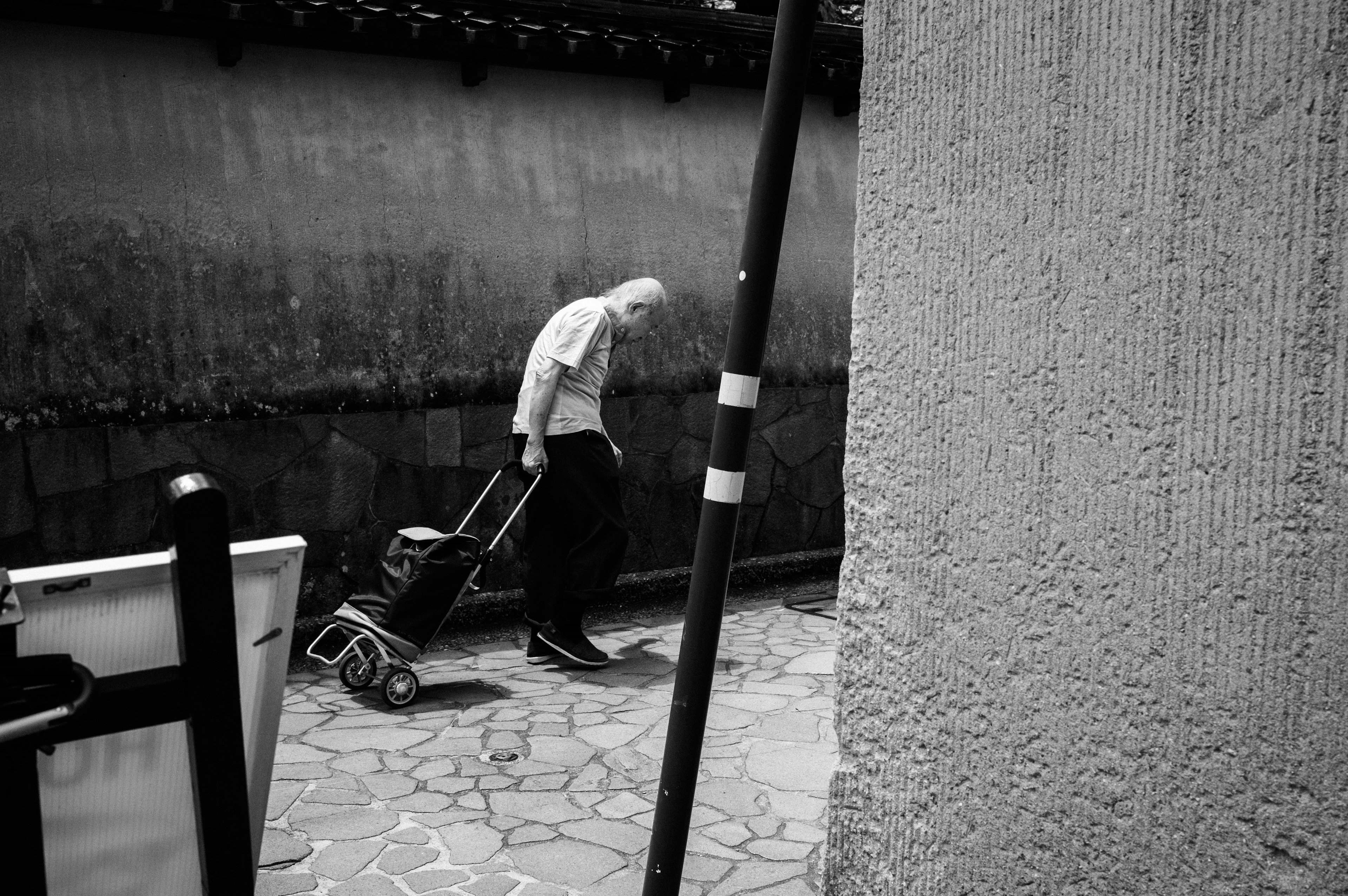 Foto en blanco y negro de un anciano caminando con un carrito por un camino estrecho