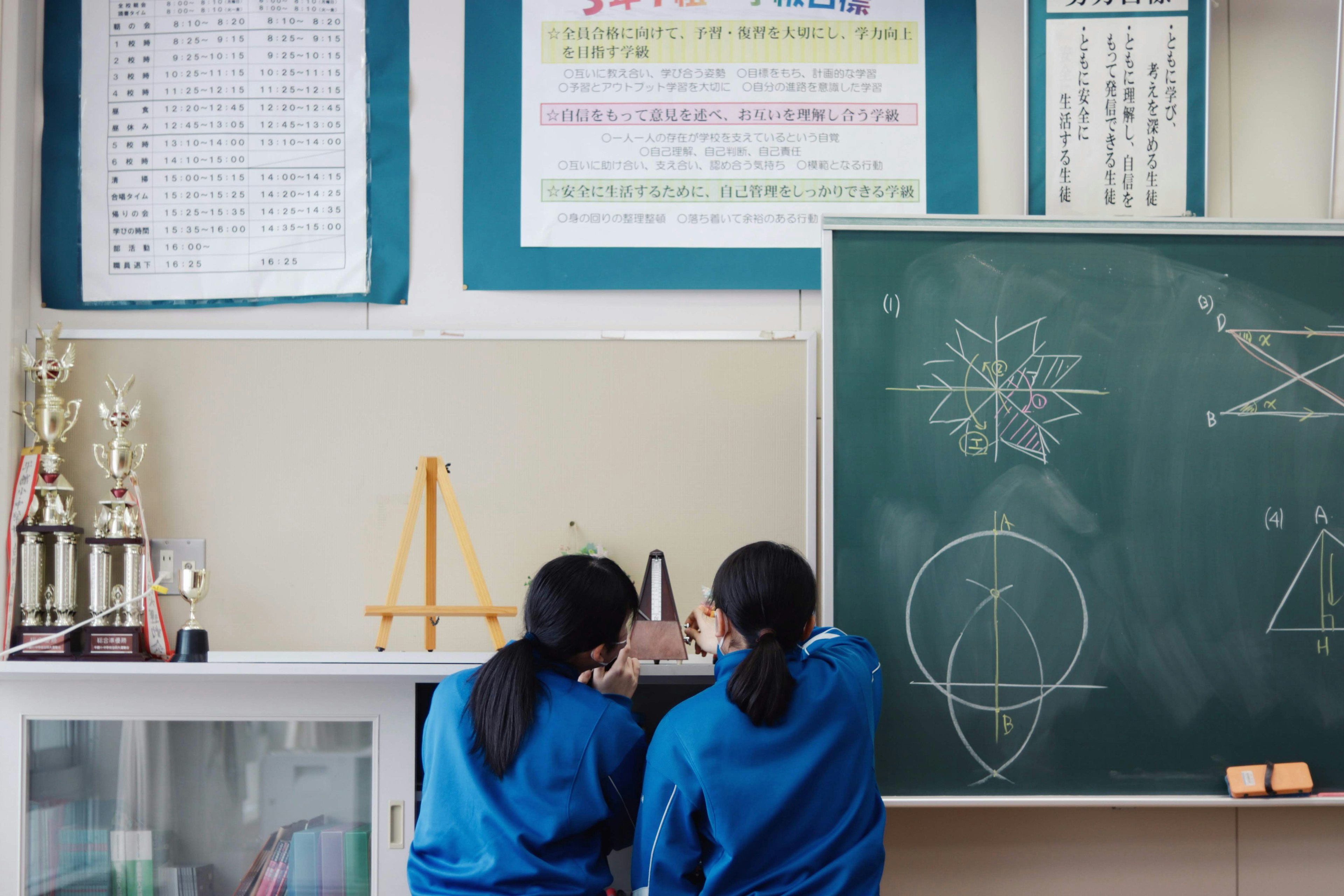 Two students standing in front of a blackboard in a classroom looking at mathematical formulas