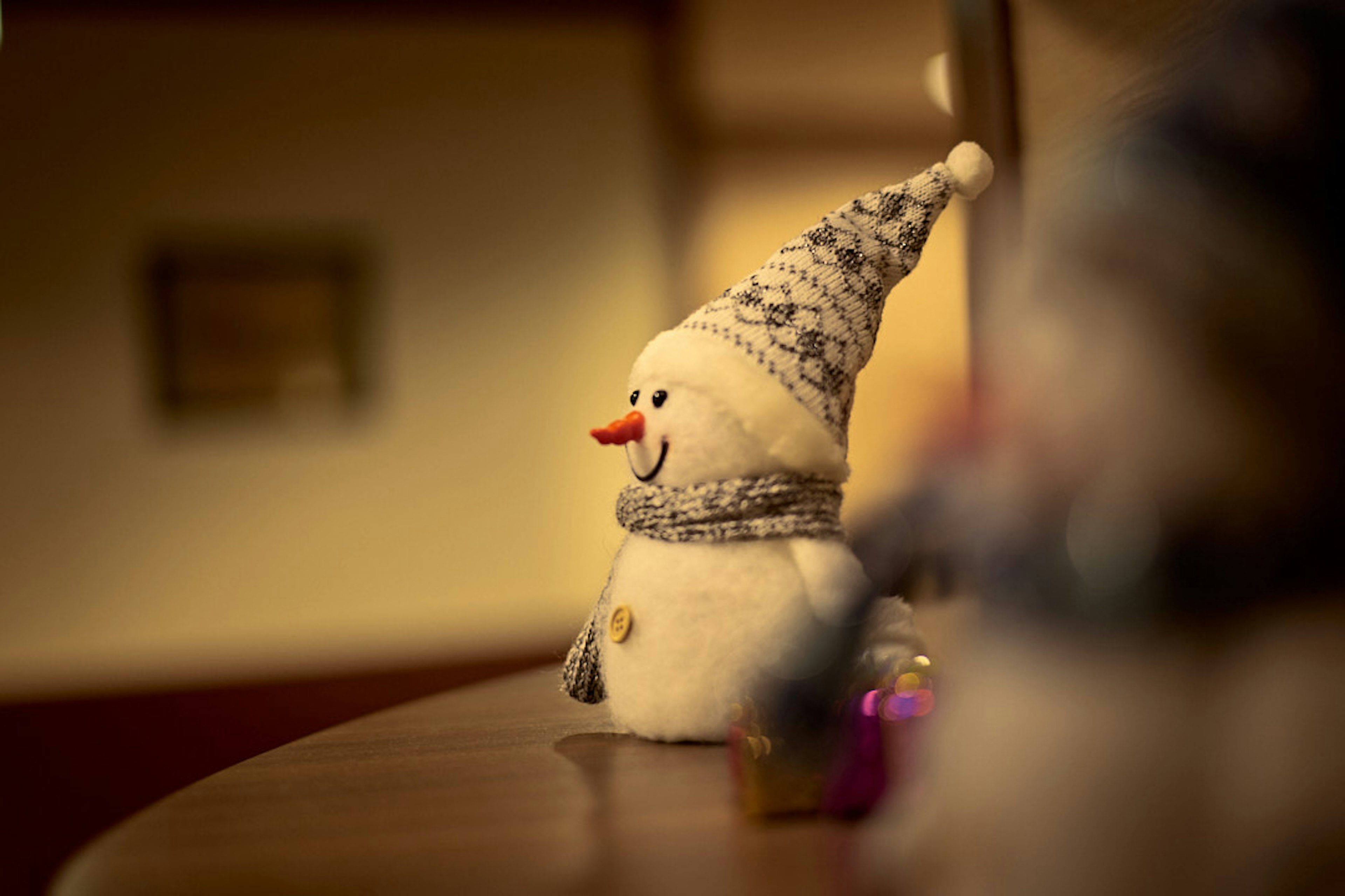 A snowman decoration with a knitted hat and scarf in a warm indoor setting