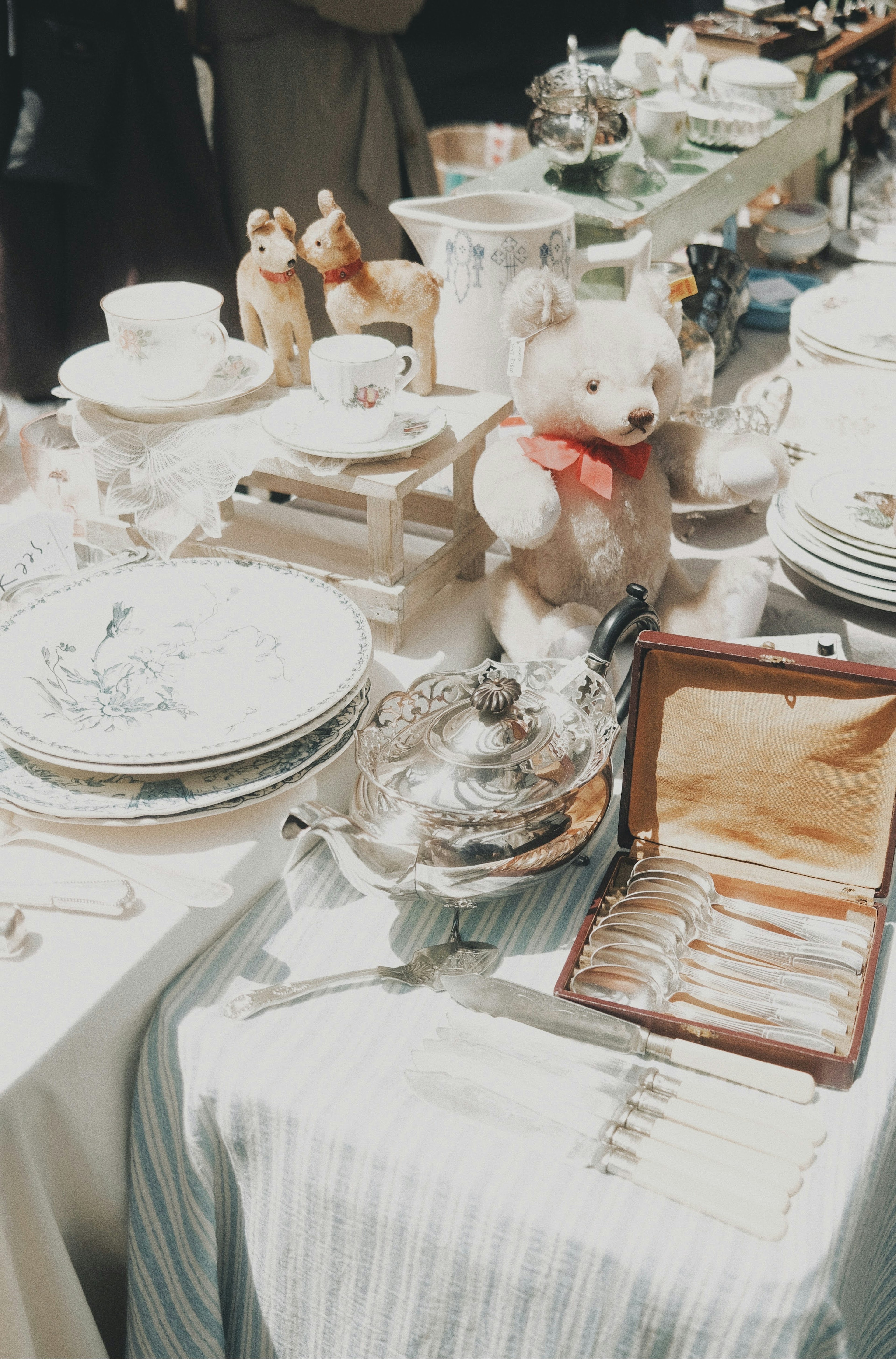 Vajilla antigua, oso de peluche, cubiertos de plata, platos blancos sobre una mesa