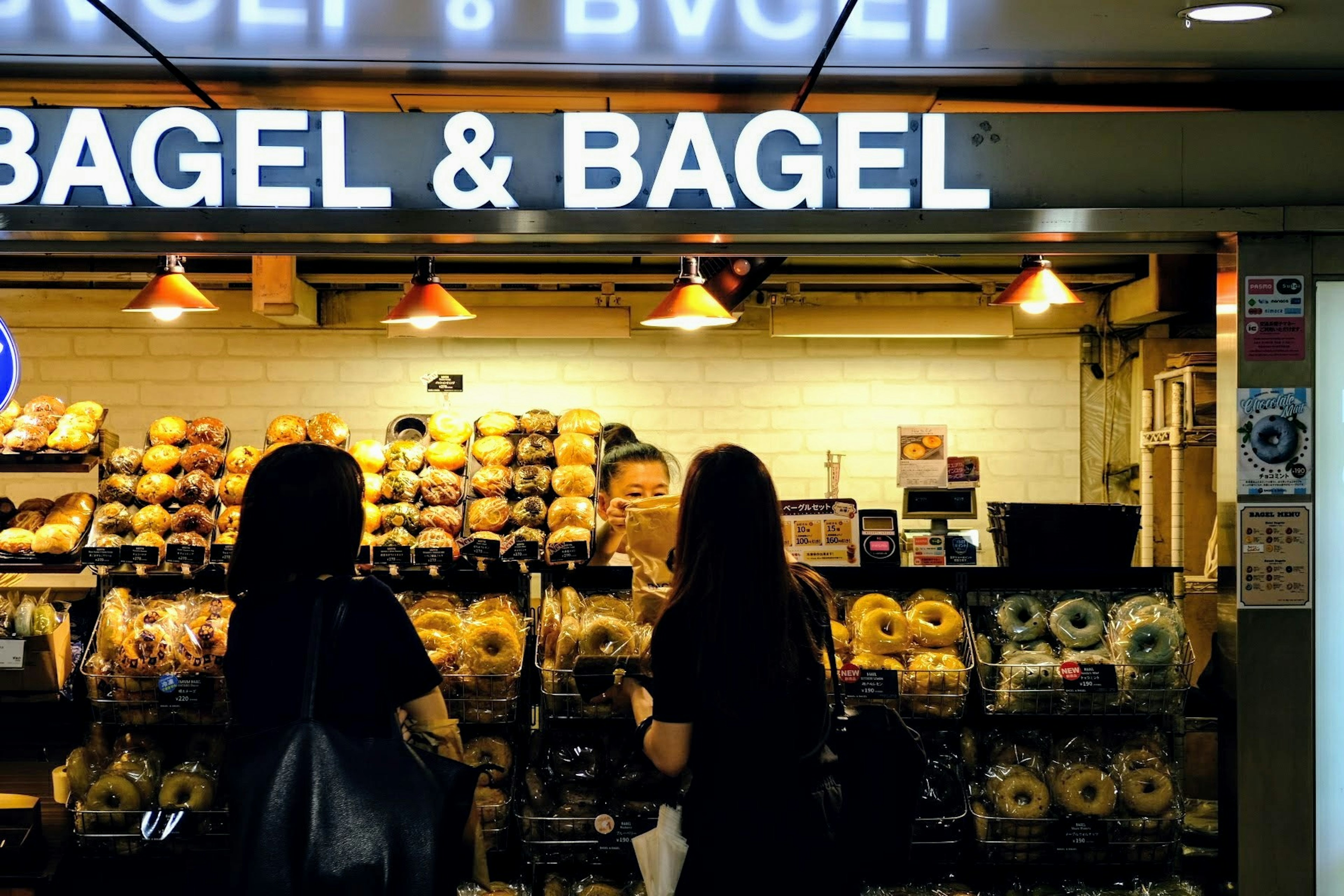 Zwei Frauen in schwarzer Kleidung, die Bagels in einem Bagel & Bagel Laden betrachten