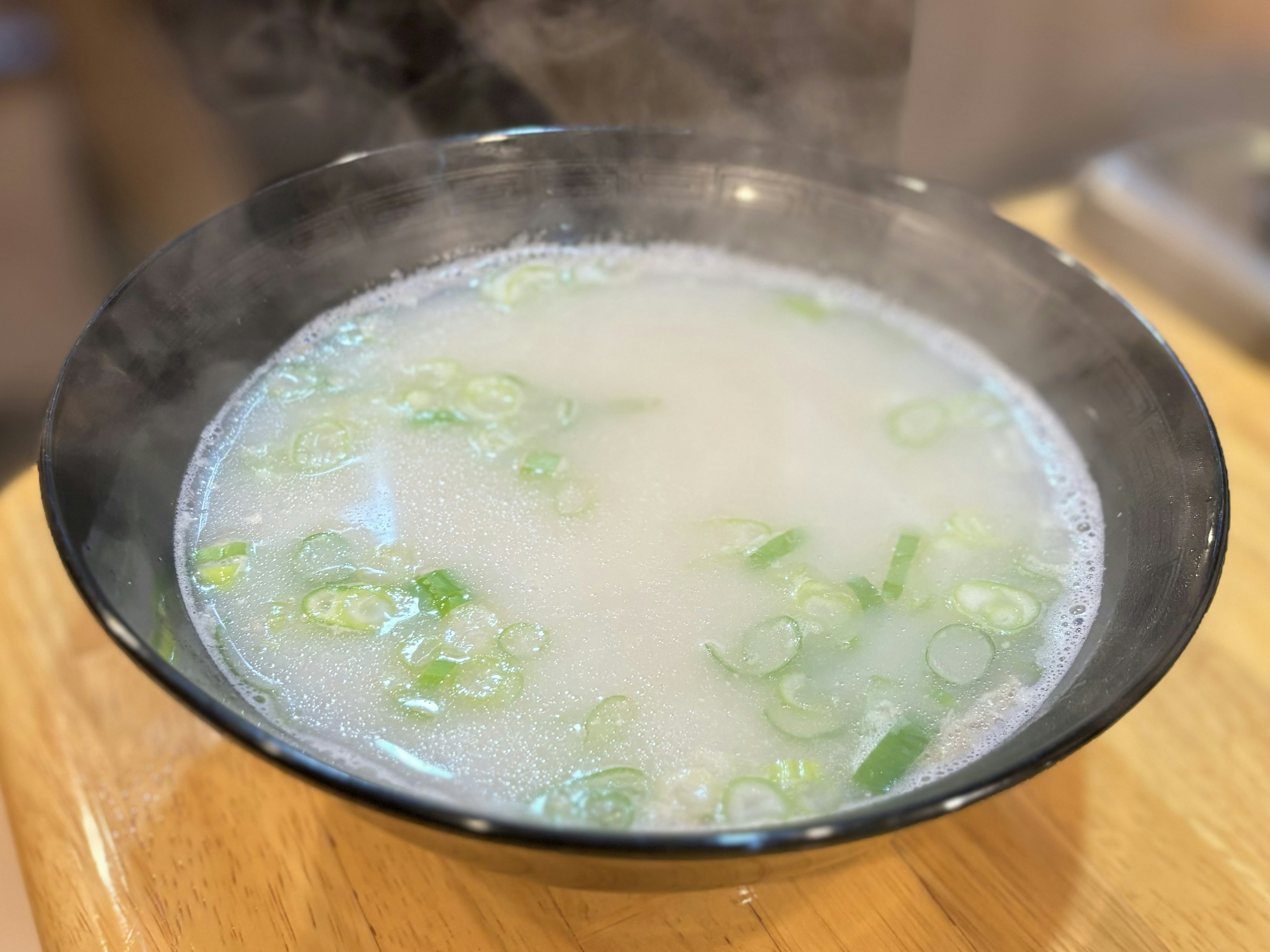 Tazón humeante de caldo con cebollitas verdes encima