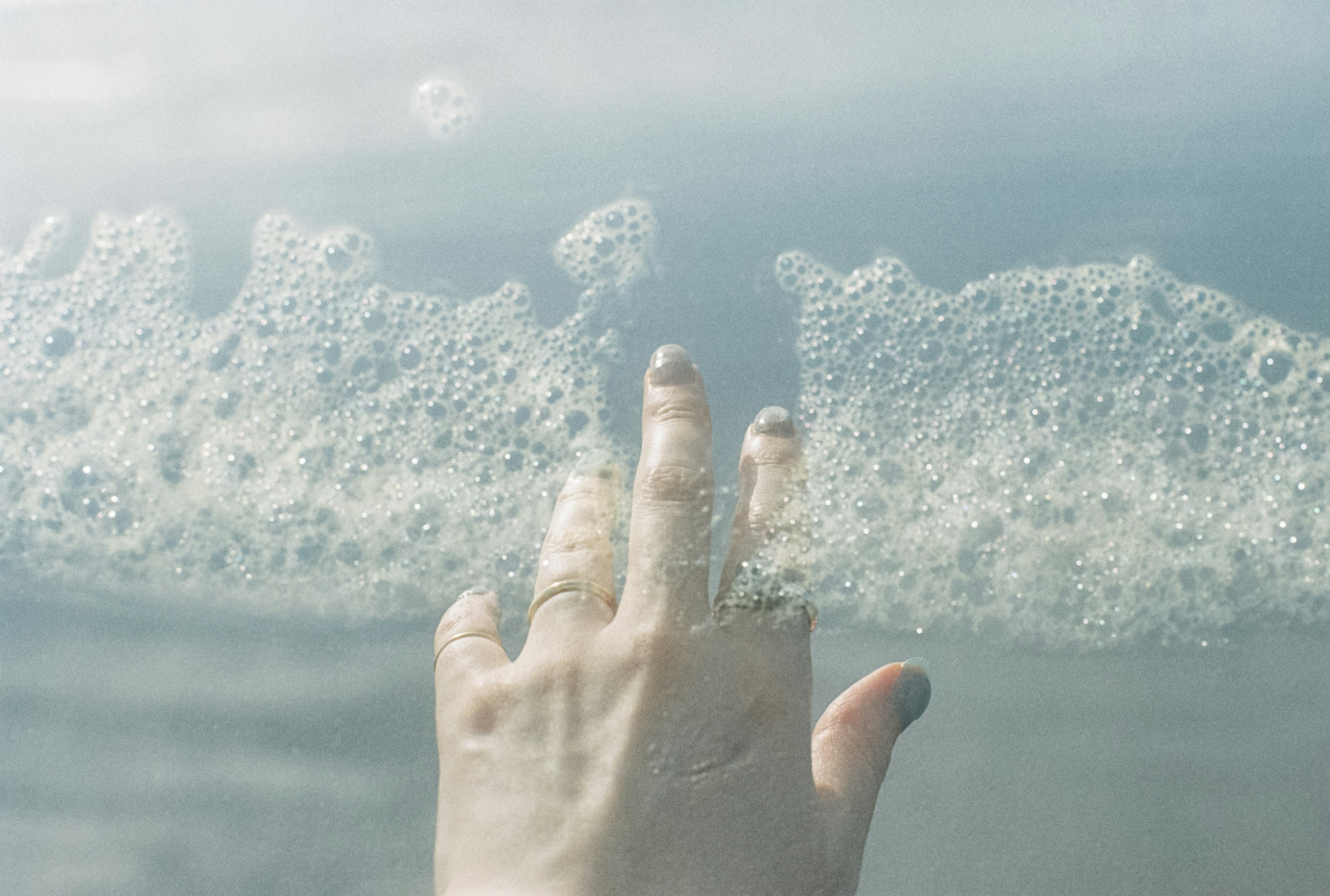 A hand reaching out to touch bubbles on the water surface