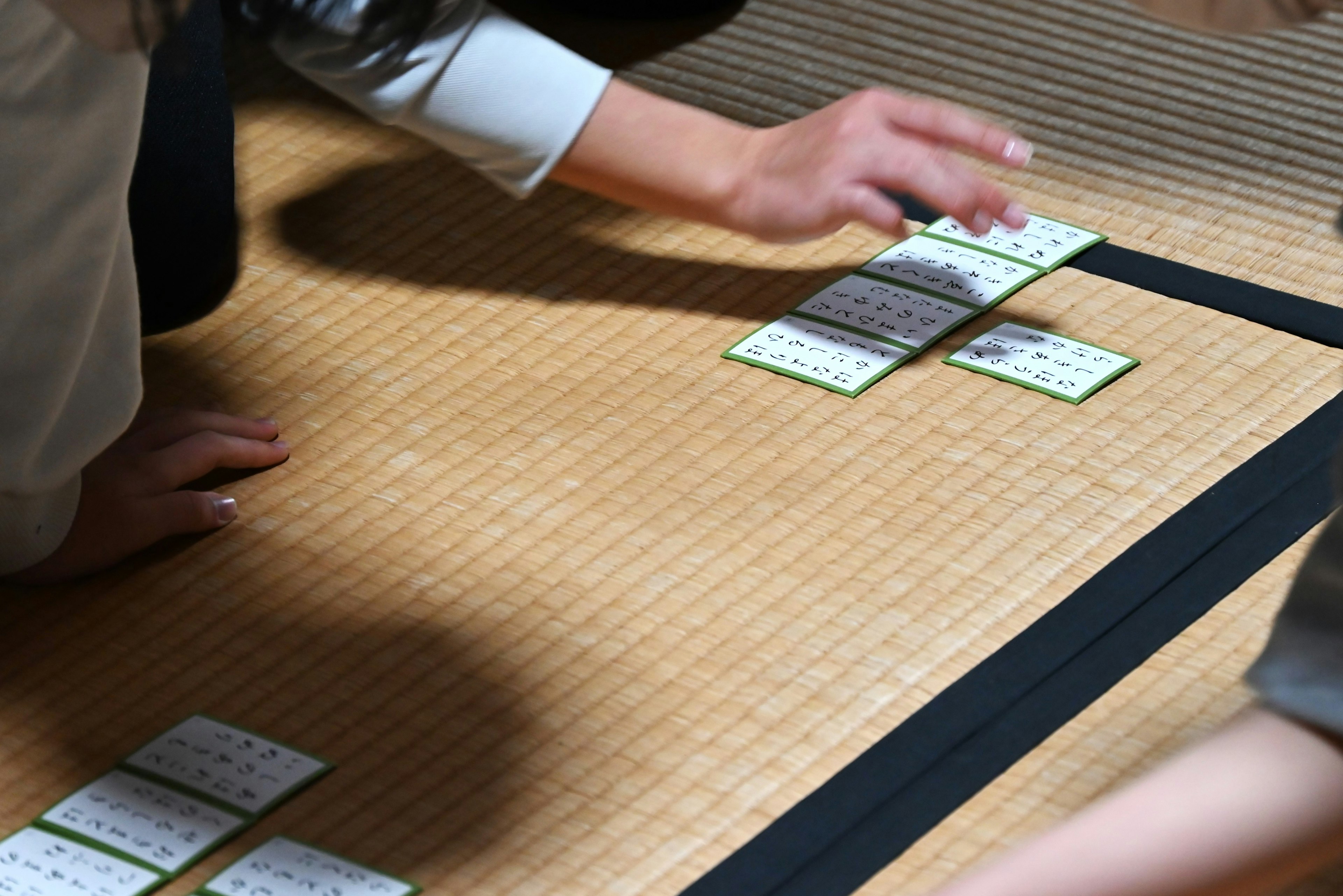 Mani di persone che giocano a un gioco di carte su pavimento in tatami