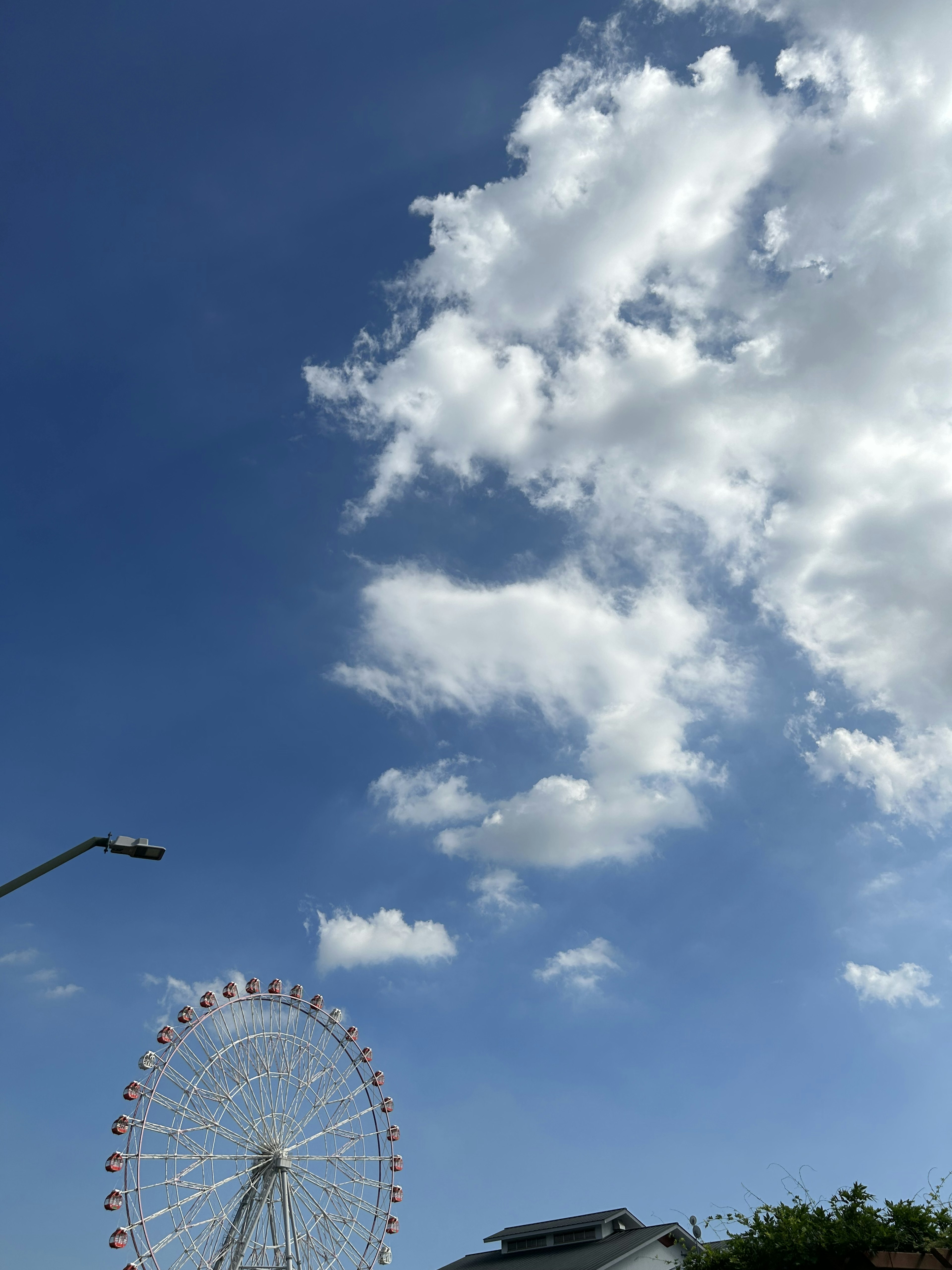 Pemandangan roda ferris di bawah langit biru dengan awan putih