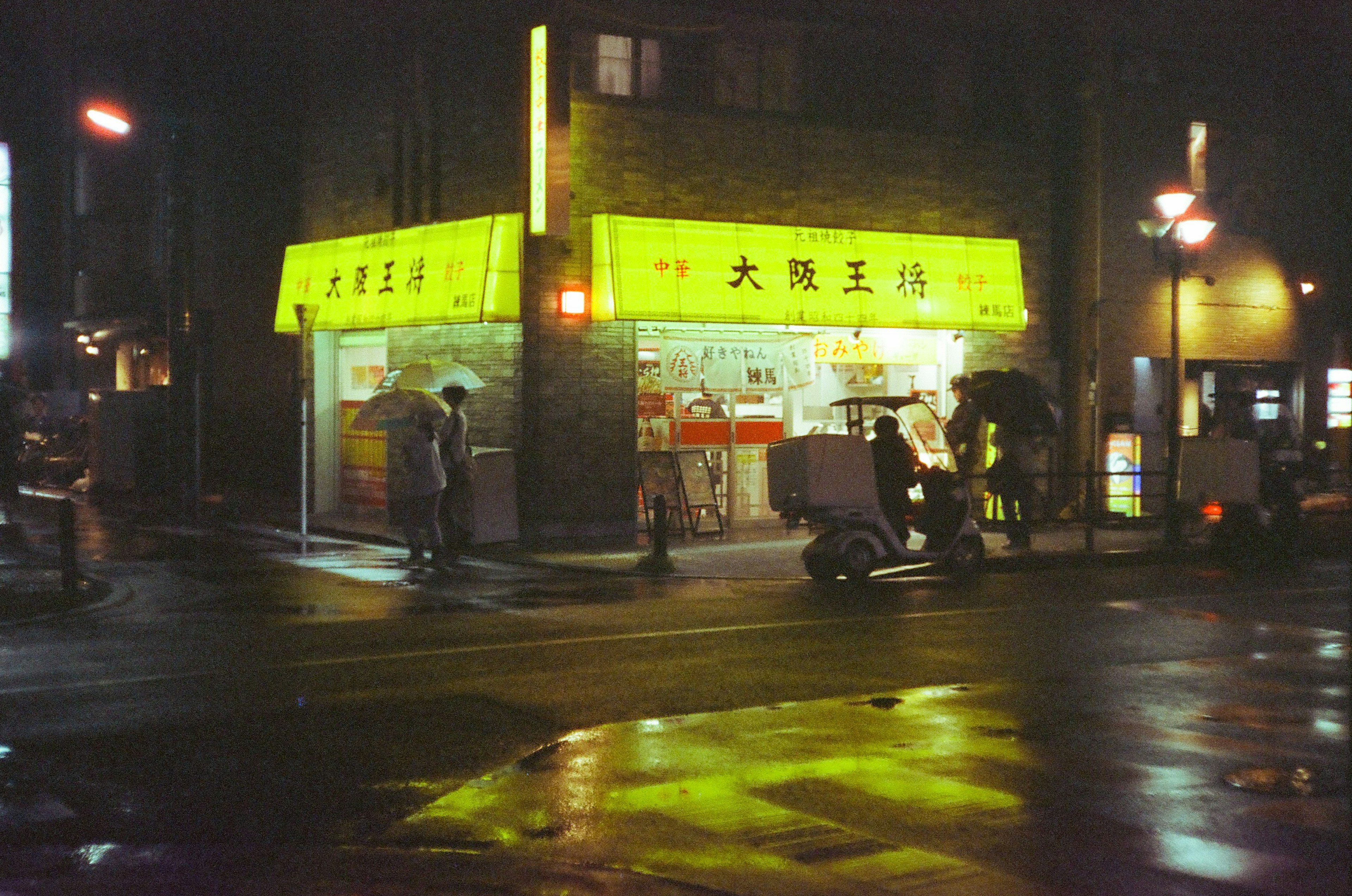 Magasin éclairé en jaune vif la nuit avec des gens et des reflets