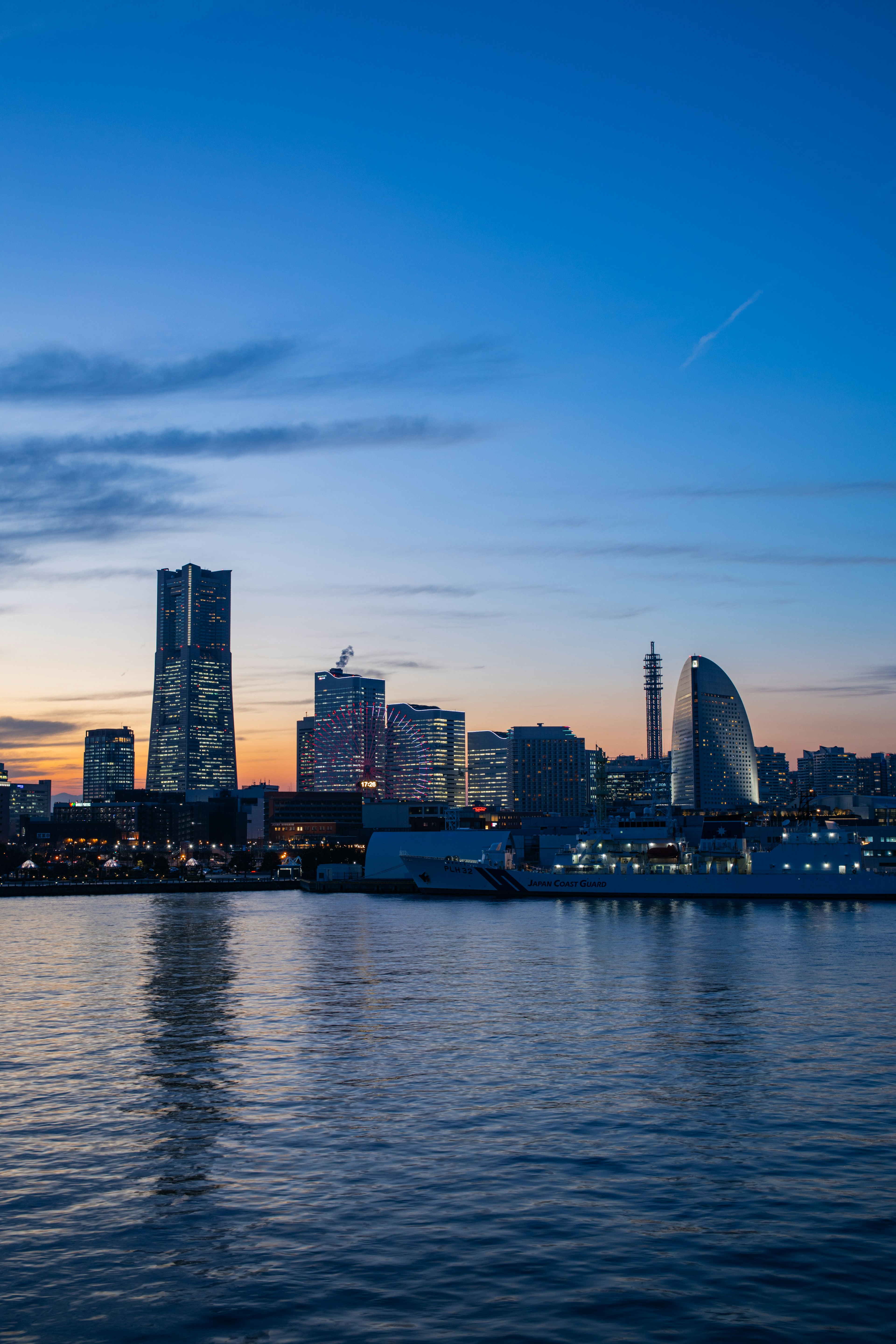 Garis langit Yokohama saat senja dengan gedung dan refleksi di air