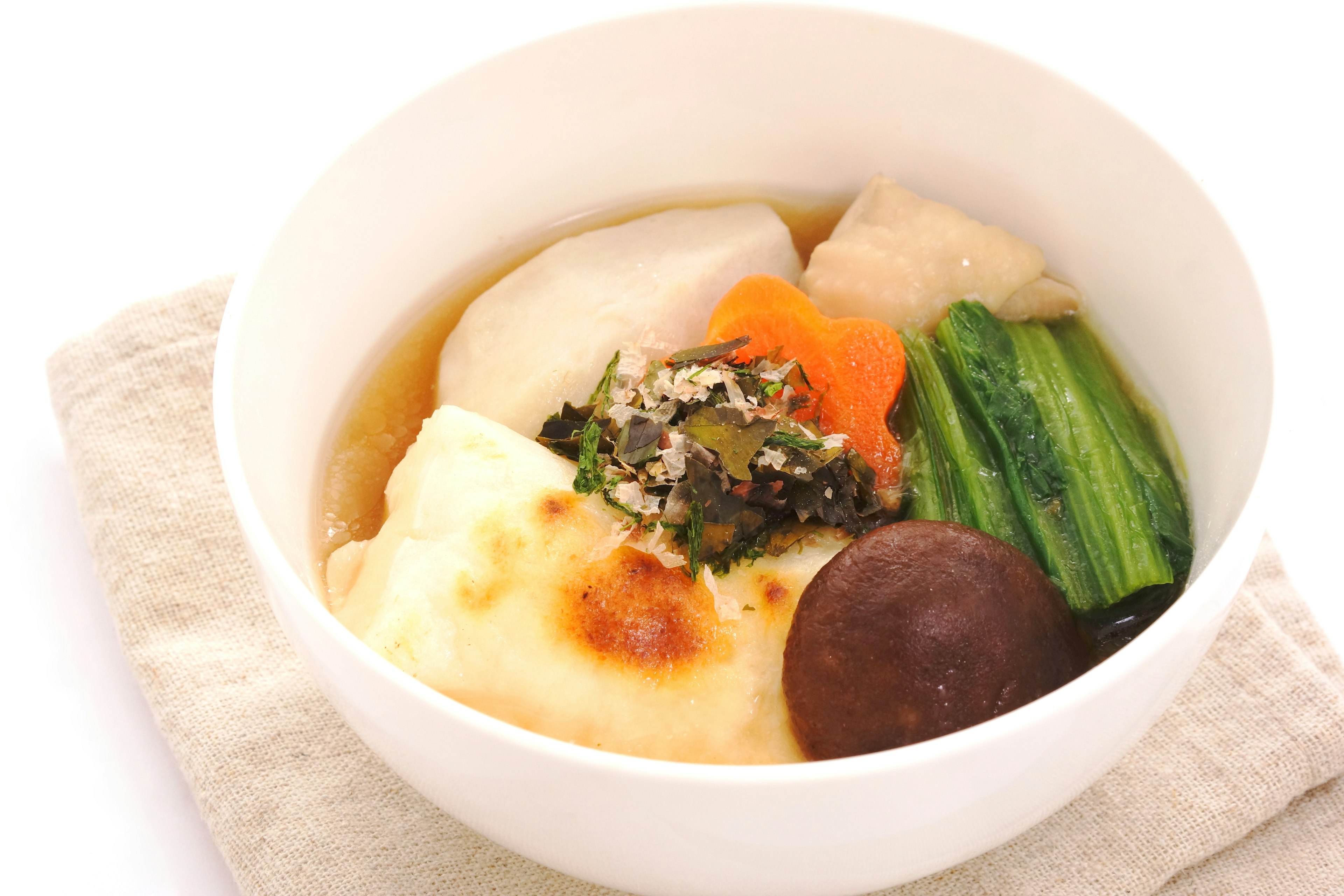 An assortment of Japanese cuisine served in a white bowl featuring soft mochi, egg, vegetables, and mushrooms