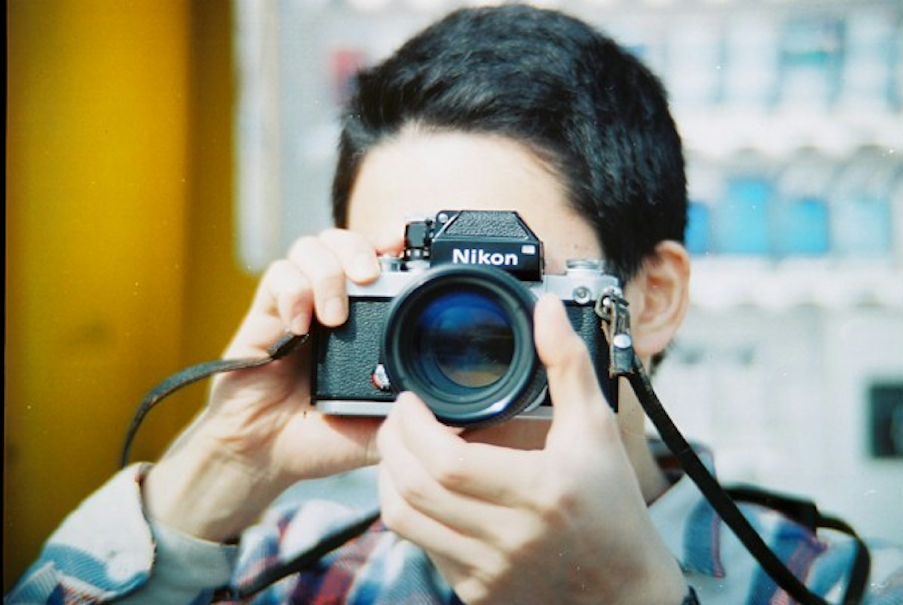 Young man holding a Nikon camera aiming at the viewer