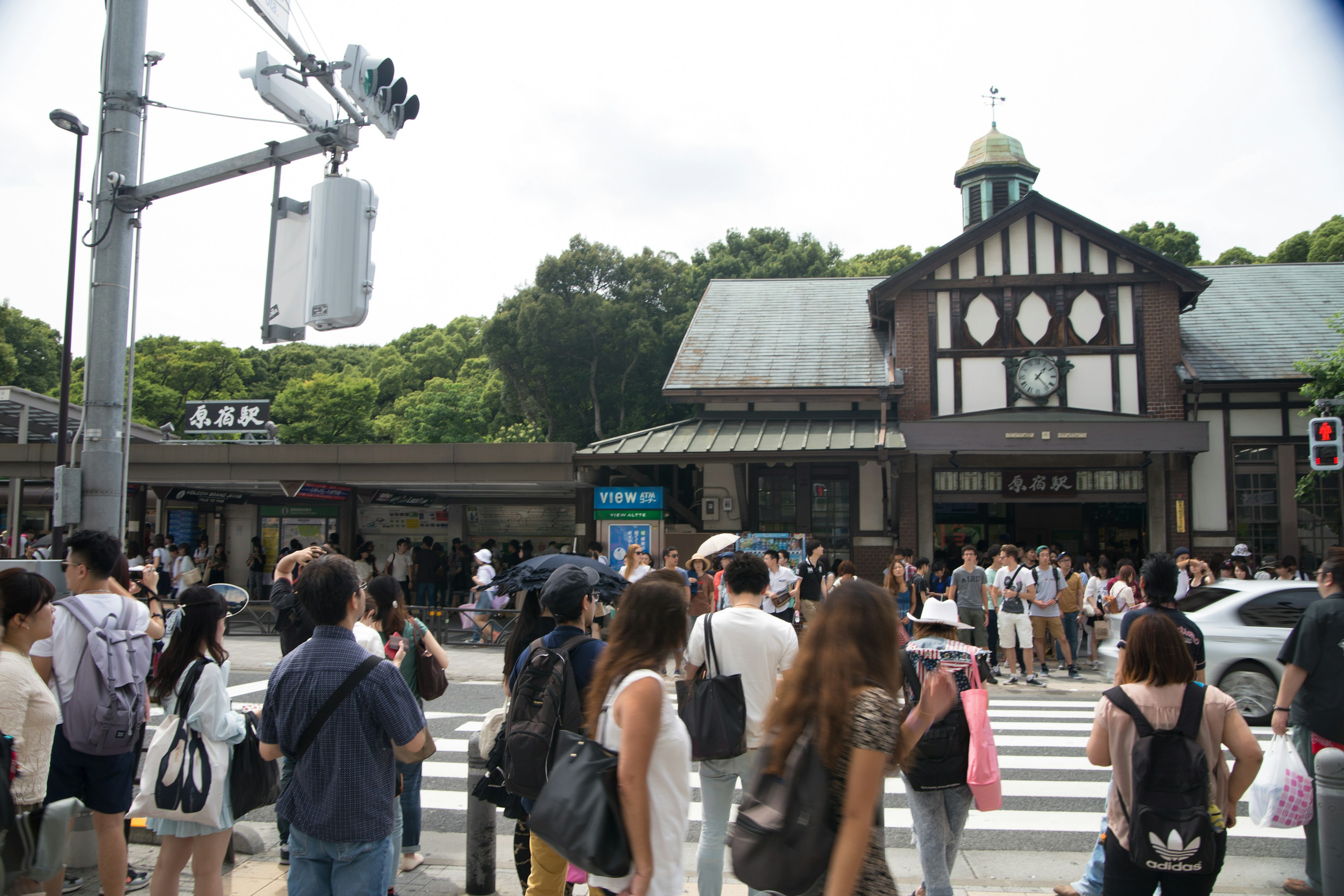 Foule traversant la rue devant une gare historique avec une verdure luxuriante