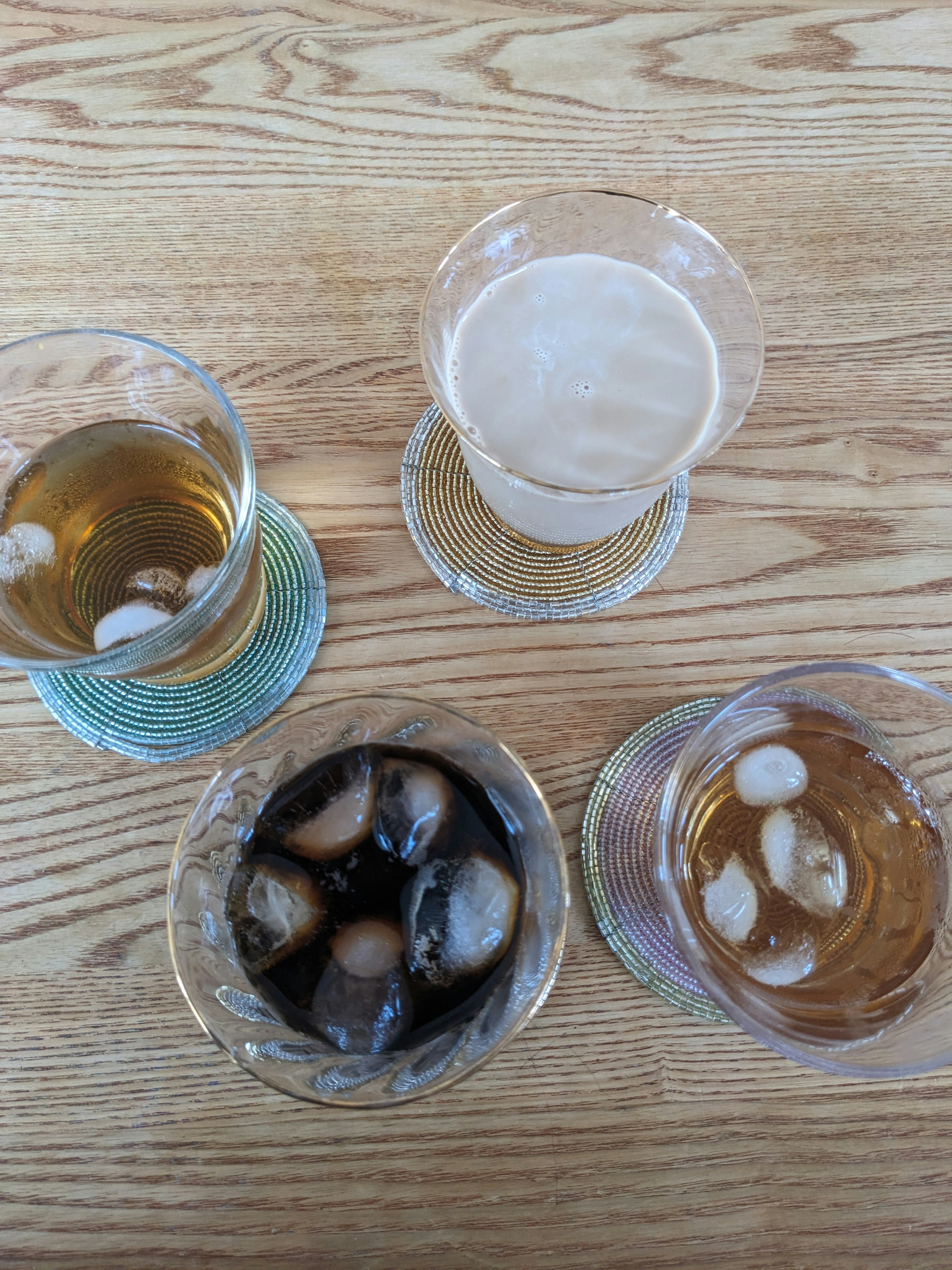 Four glasses with drinks and ice placed on a wooden table