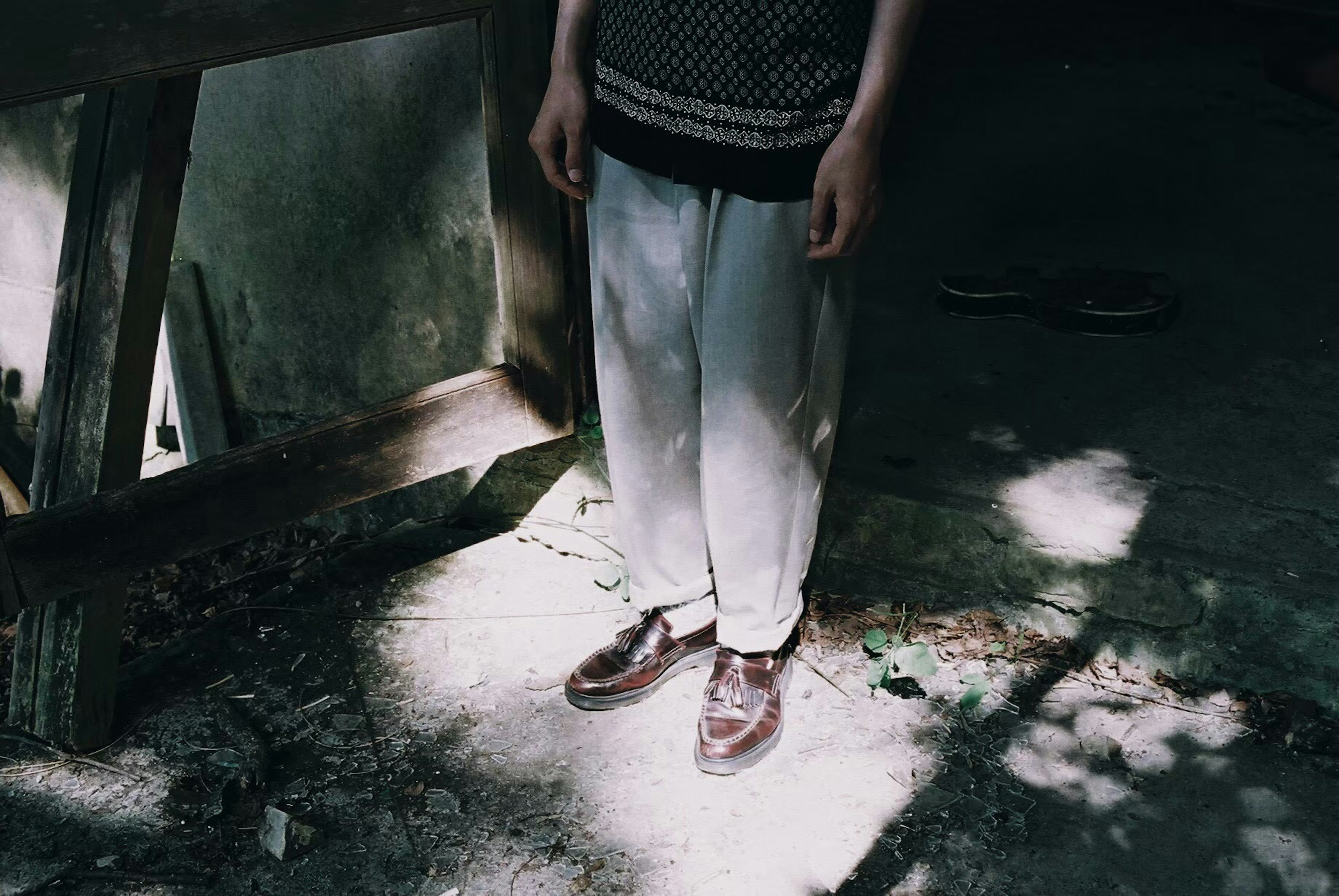 A person standing in a dimly lit area showcasing their feet wearing light-colored pants and shoes