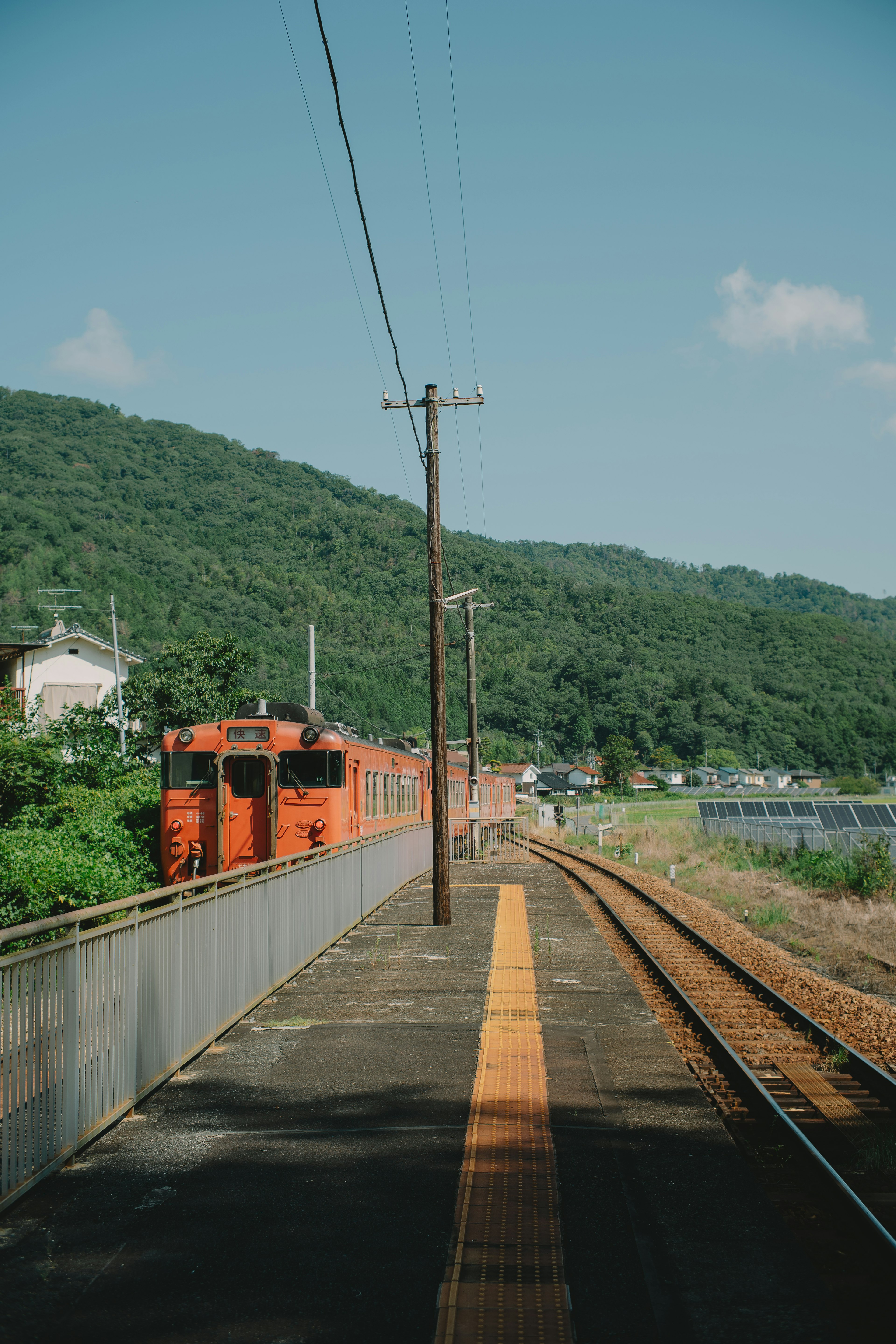 Orange train at a station with green mountains in the background