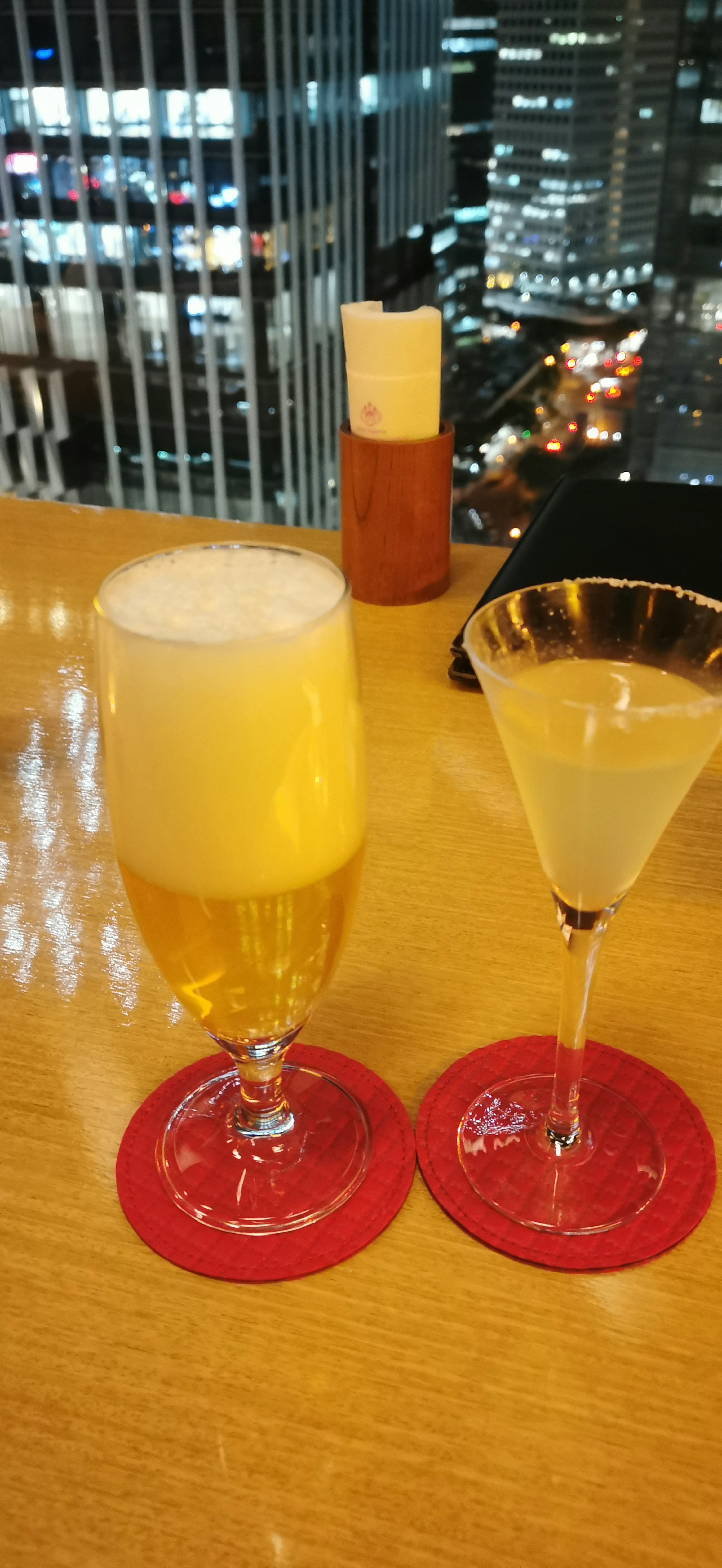 A glass of beer and a martini on a table with a city skyline in the background