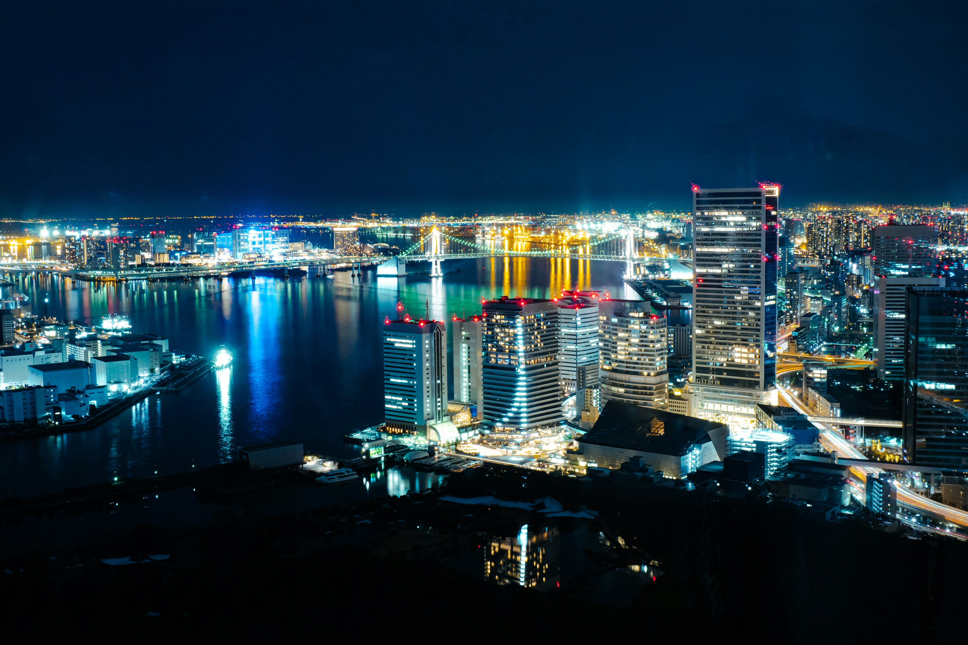 Atemberaubende Panoramaansicht einer Stadt bei Nacht mit beleuchteten Wolkenkratzern, die sich im Wasser spiegeln