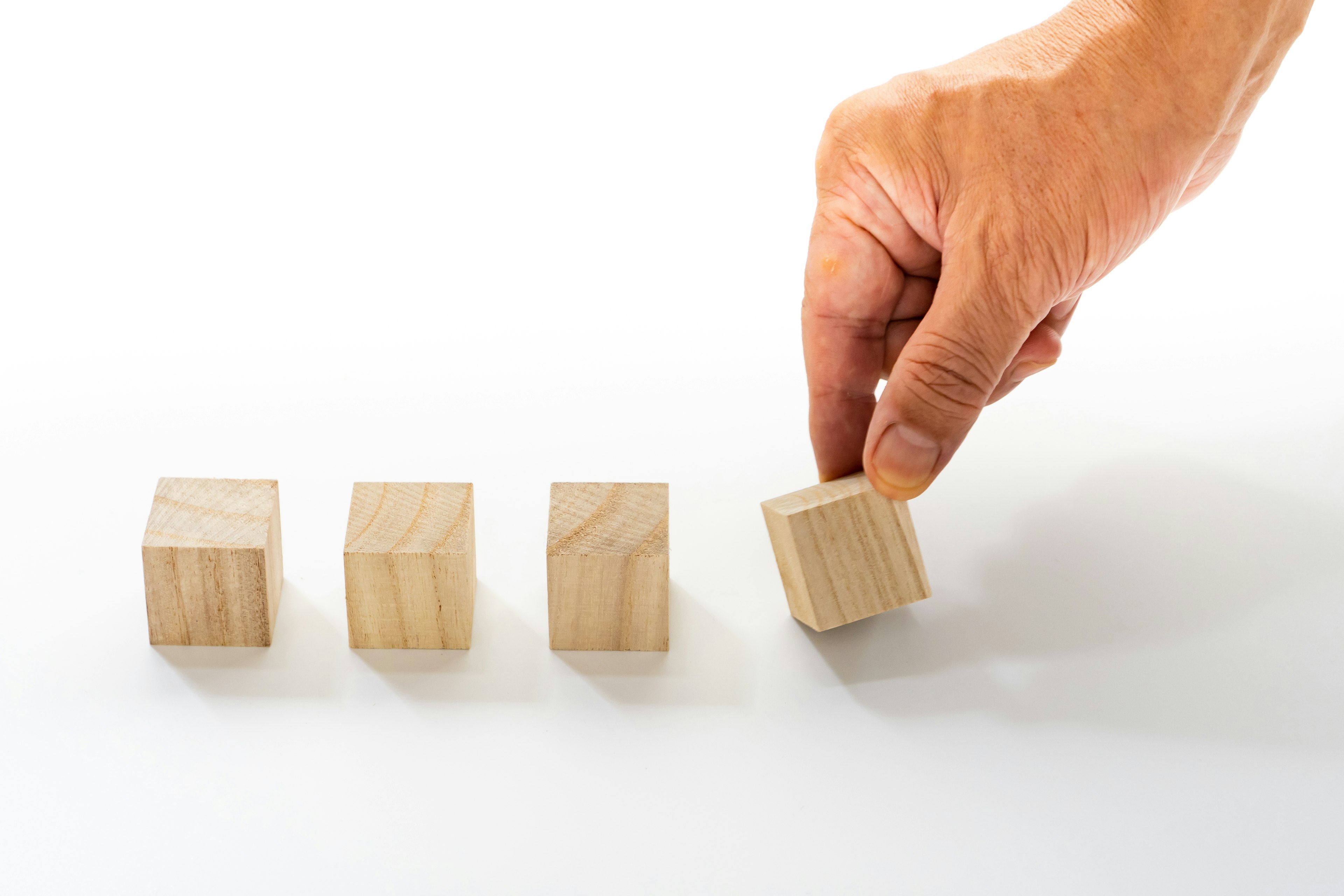 A hand holding a wooden cube next to three aligned wooden cubes