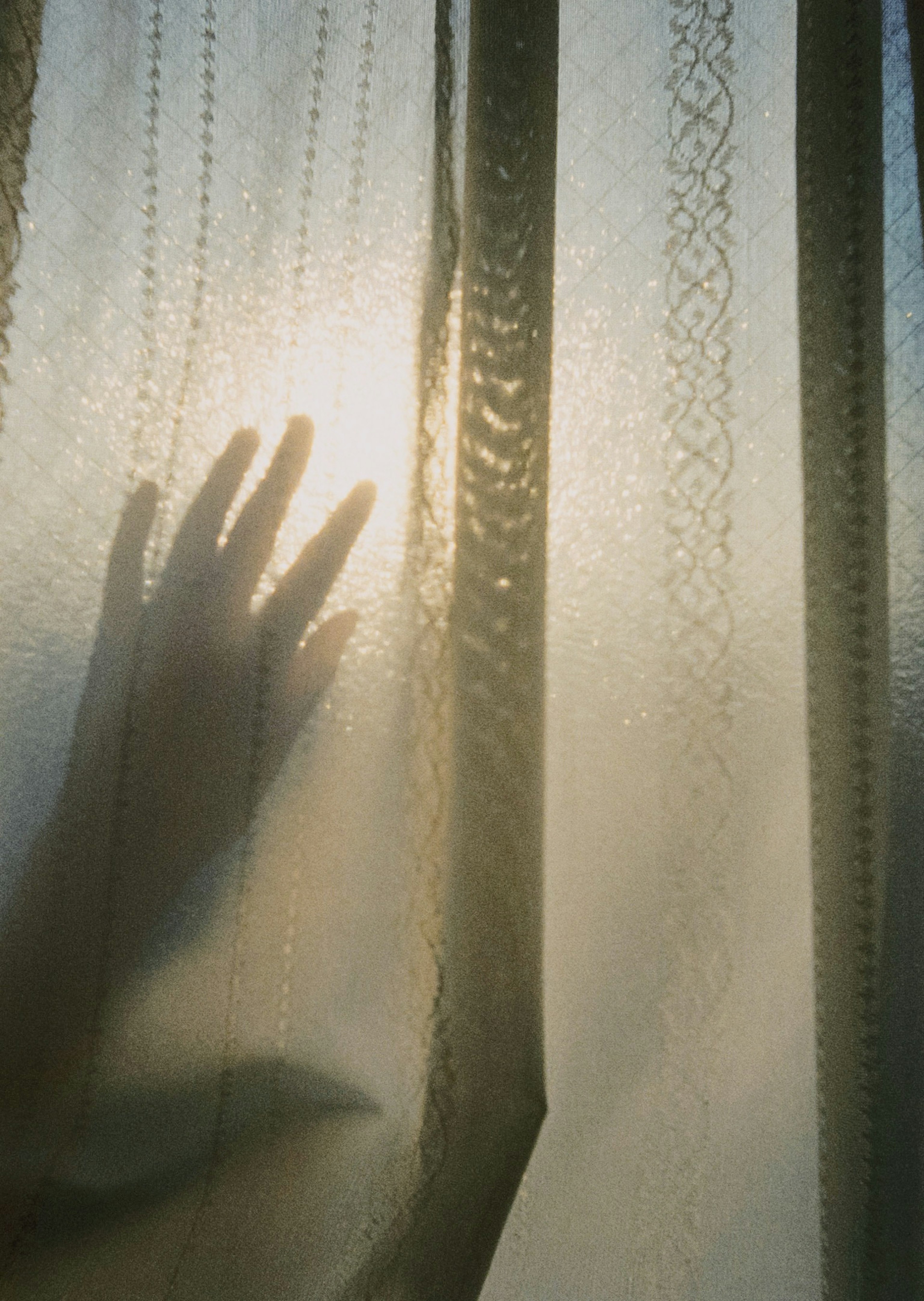 Silhouette of a hand against a sheer curtain with soft light filtering through