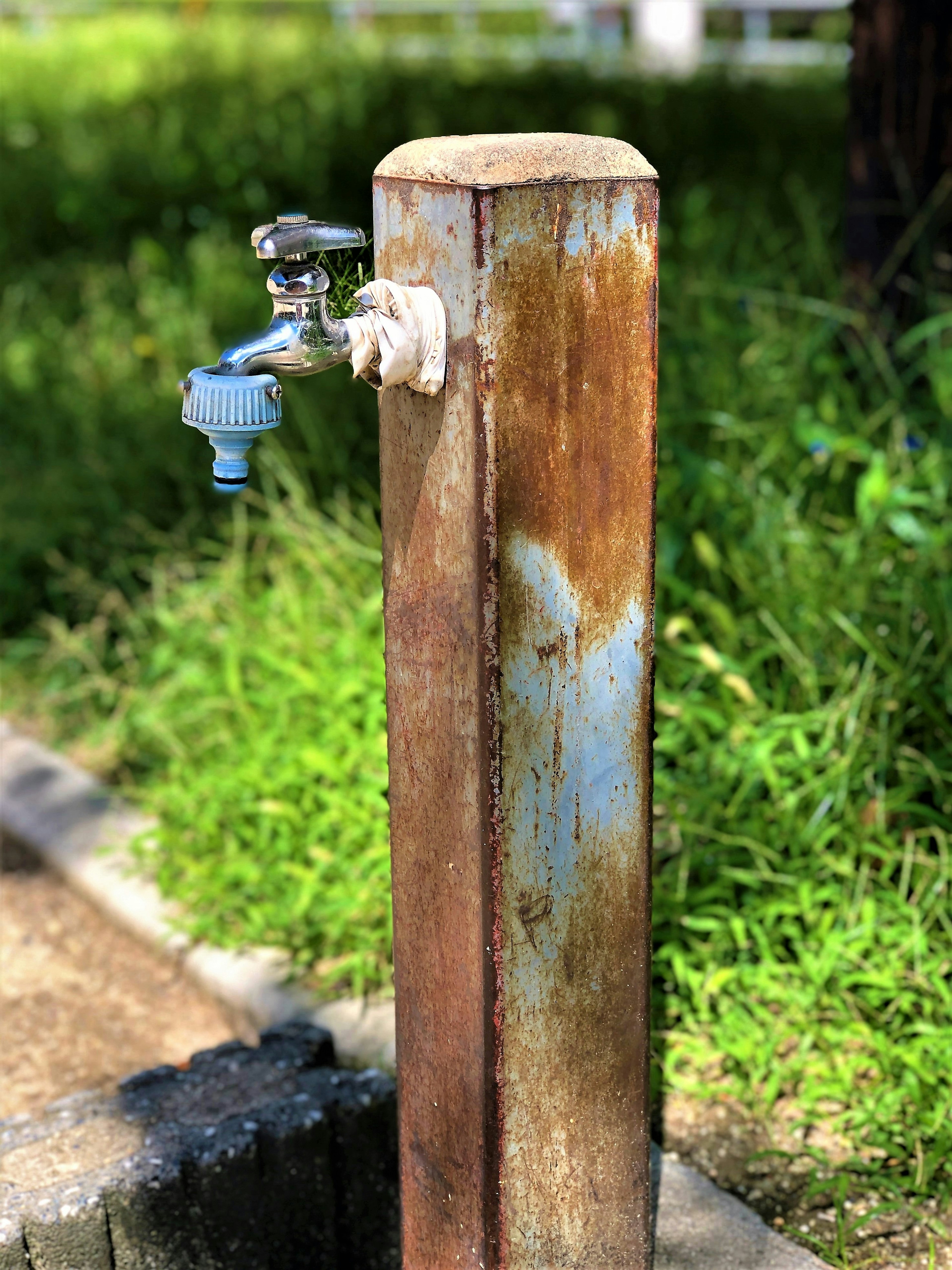 Colonna d'acqua arrugginita con un rubinetto blu in piedi nell'erba verde