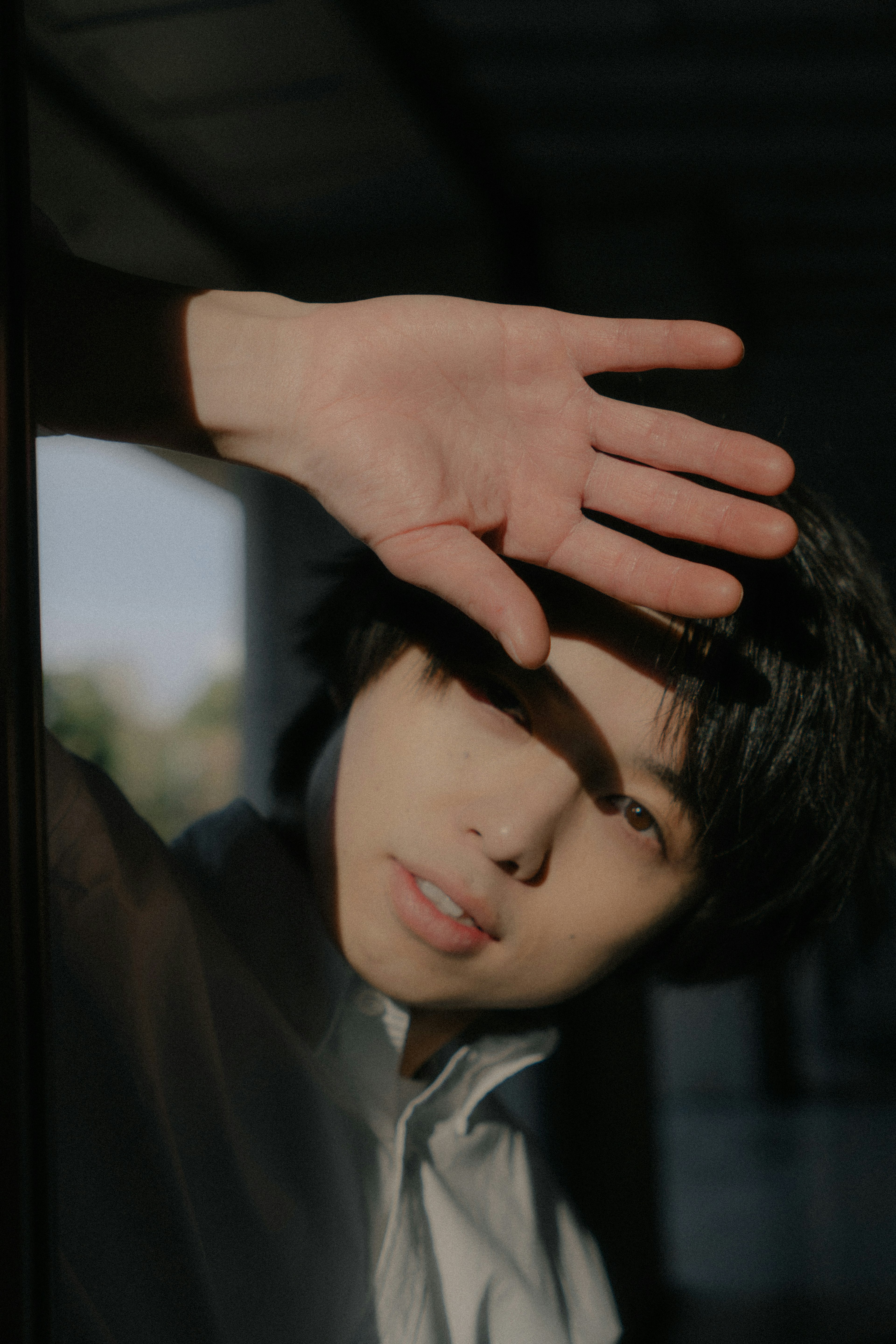 Young man standing by the window shielding his face with his hand