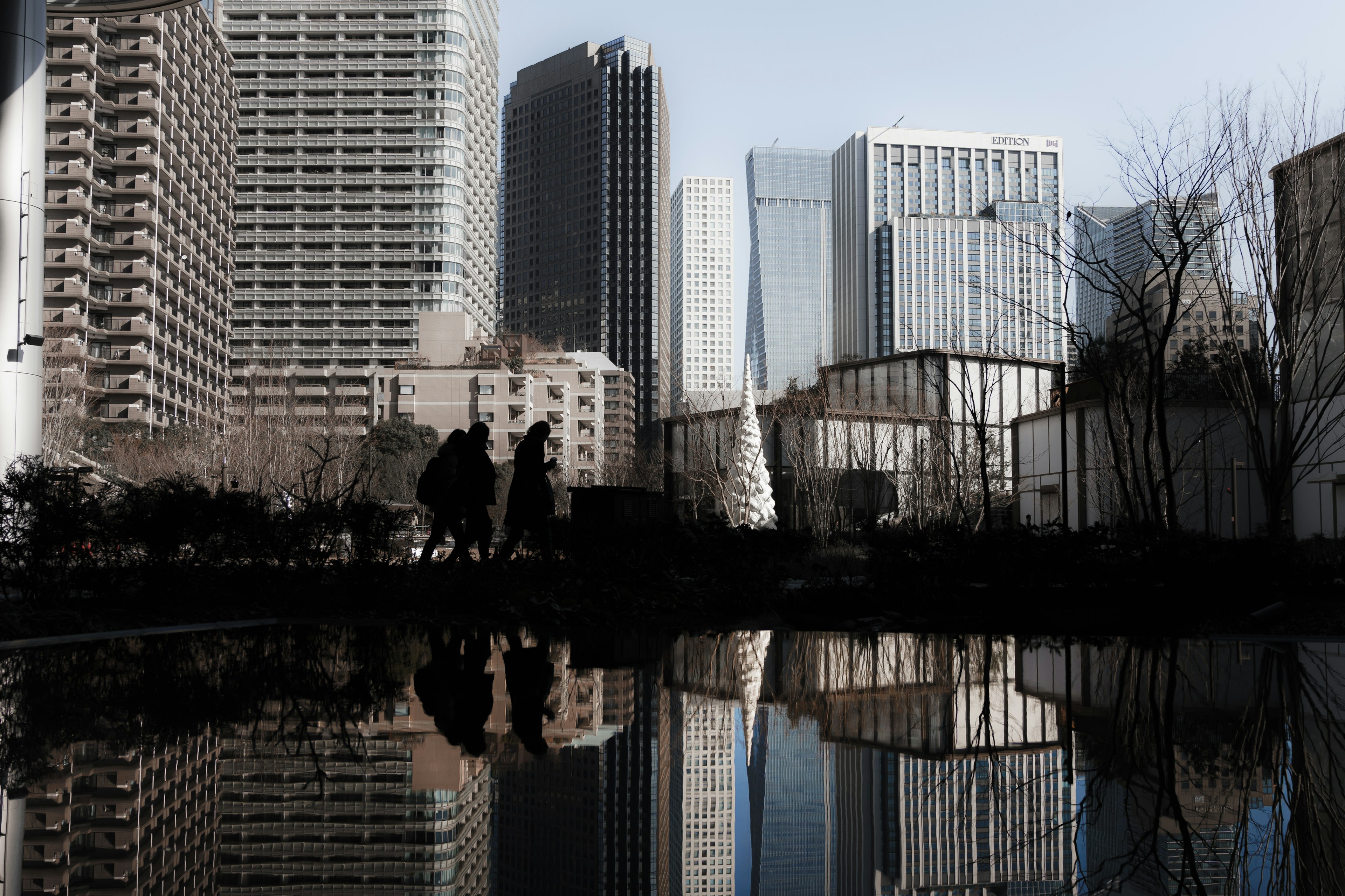 Silhouetten von Menschen, die an modernen Wolkenkratzern vorbeigehen, die im Wasser reflektiert werden