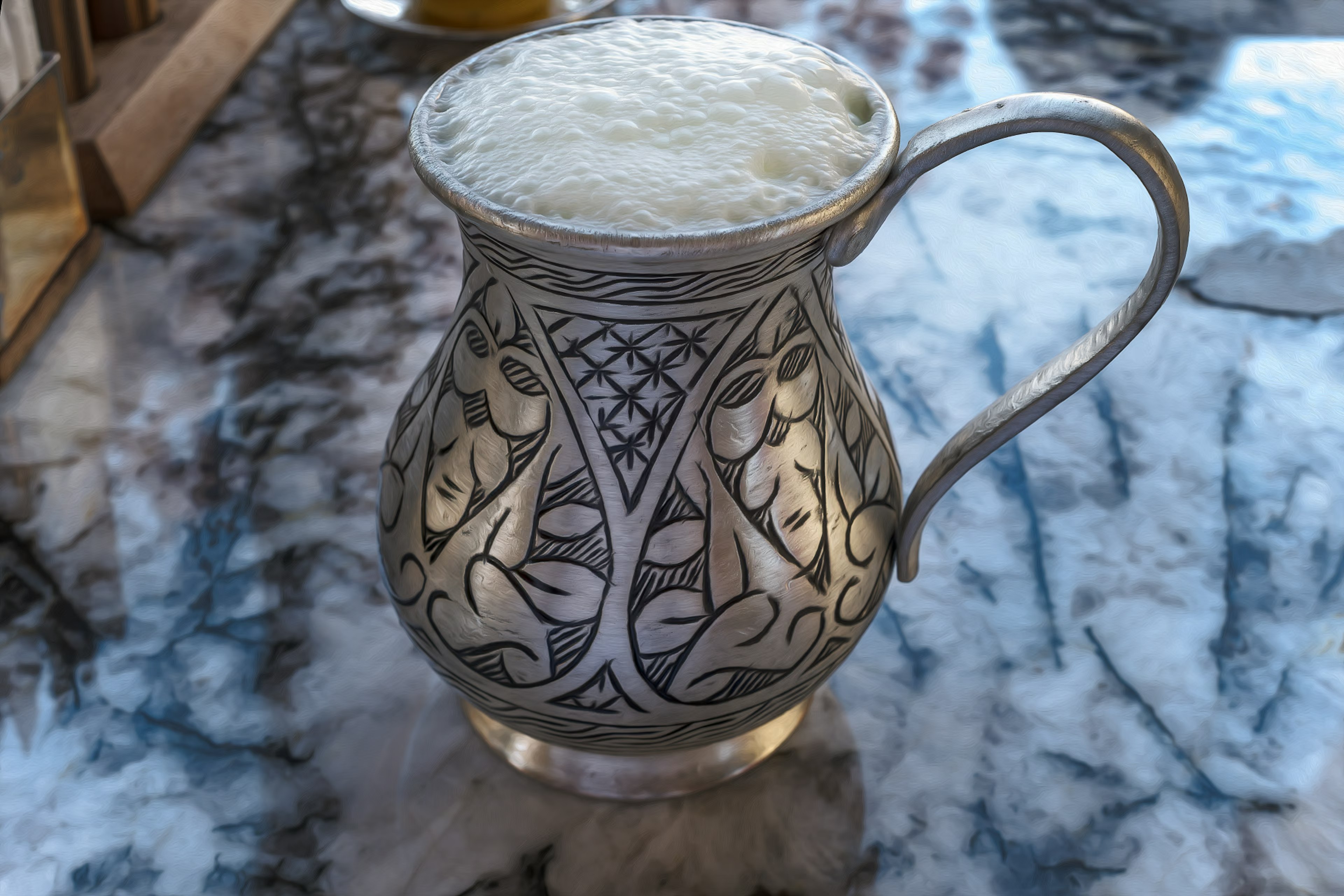 Decorative silver pitcher filled with frothy beverage