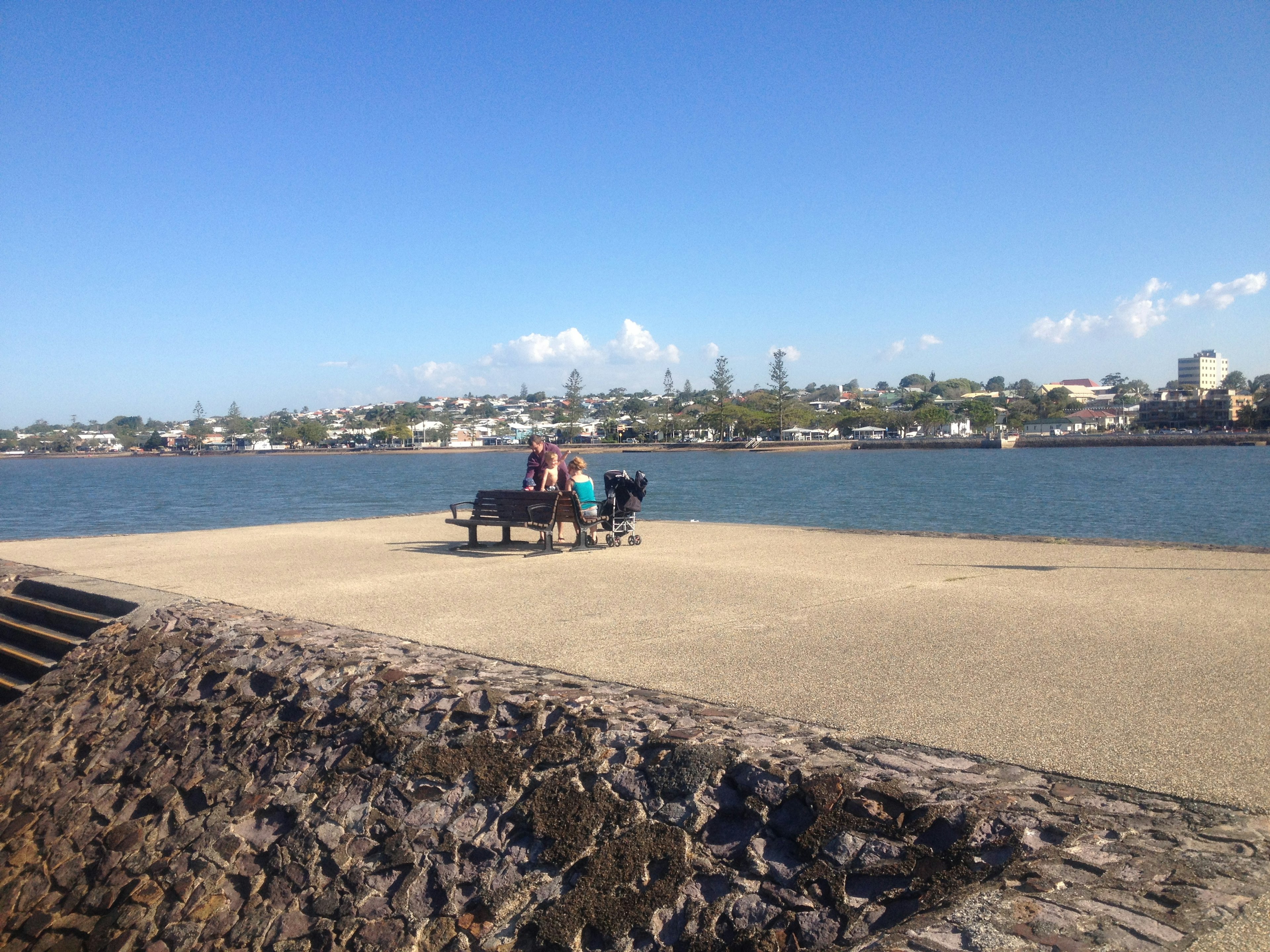 People sitting on a bench by the water with a city skyline in the background