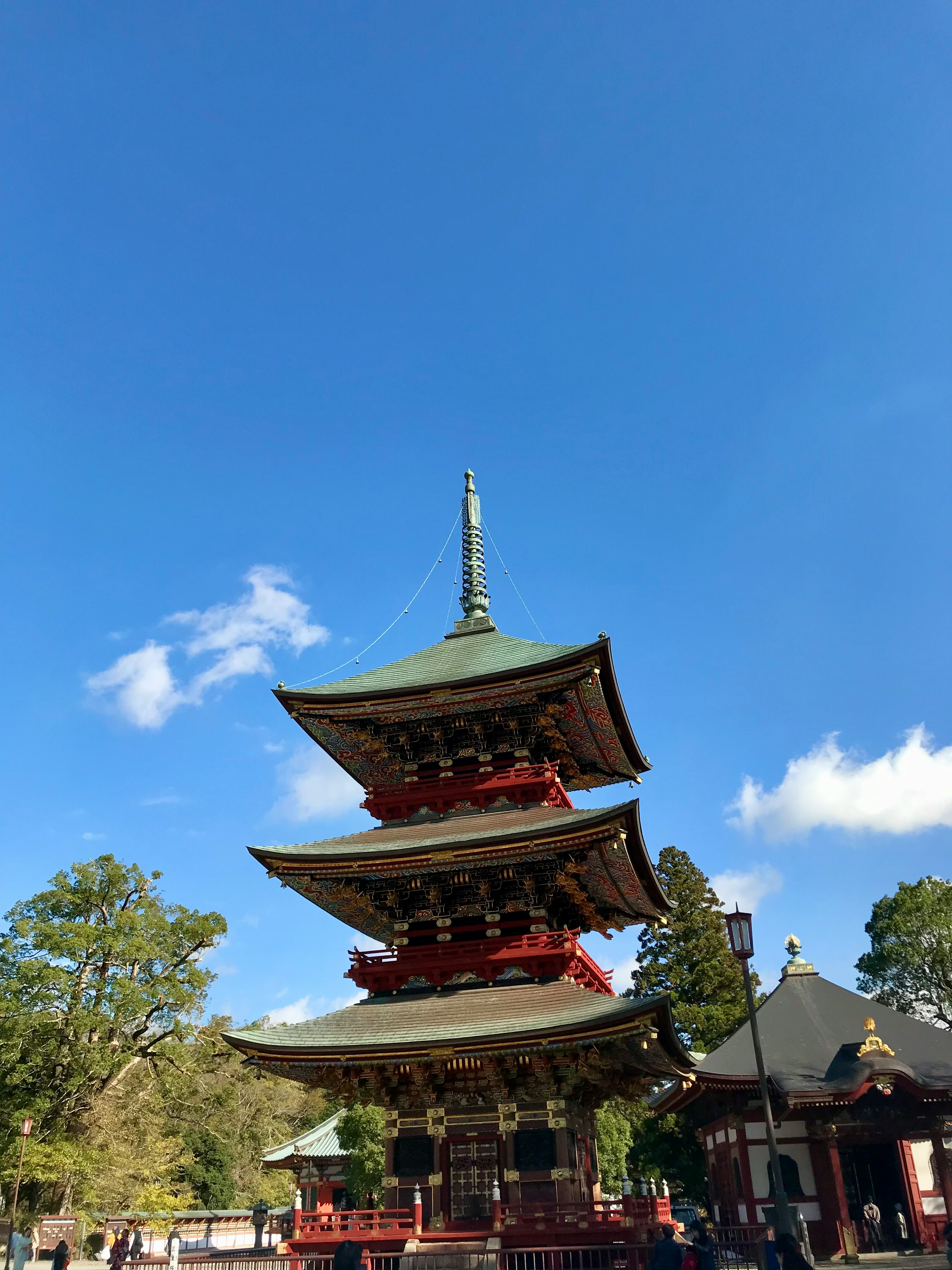 青空の下に立つ三層の塔と周囲の木々