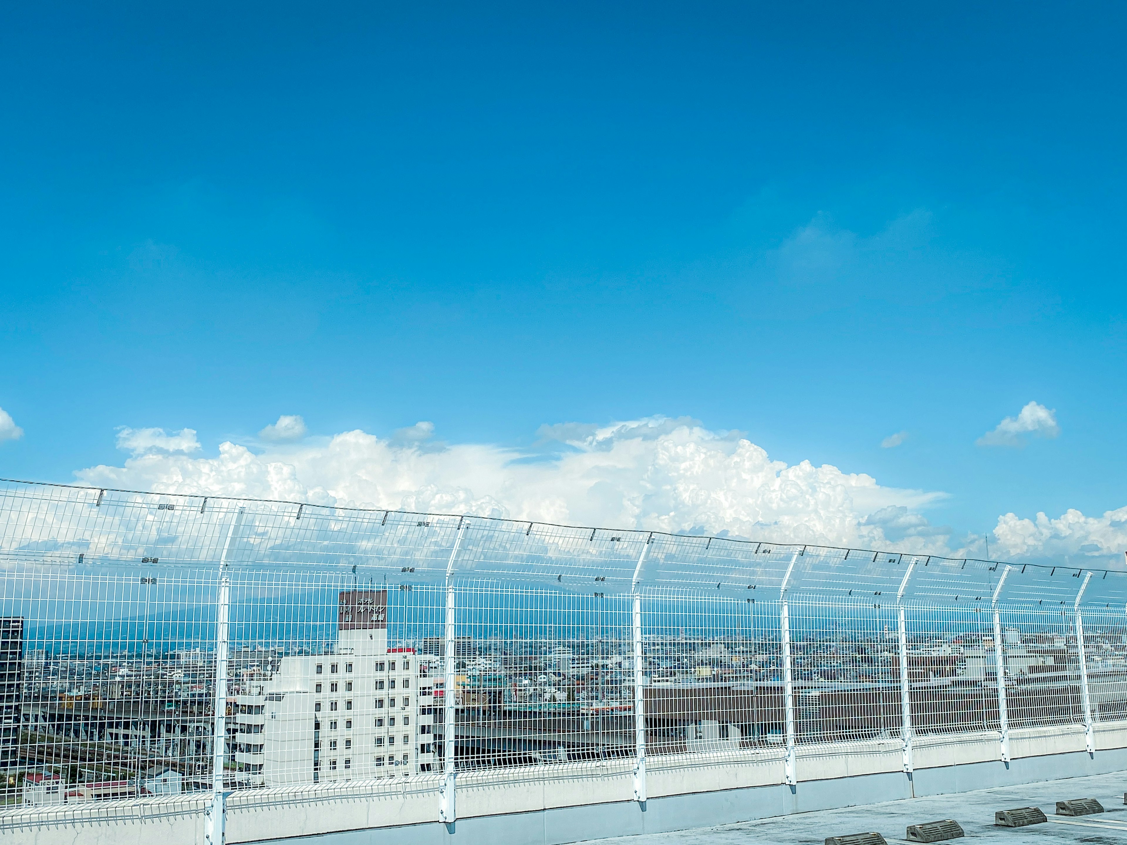 青空と白い雲が広がる都市の風景とフェンス