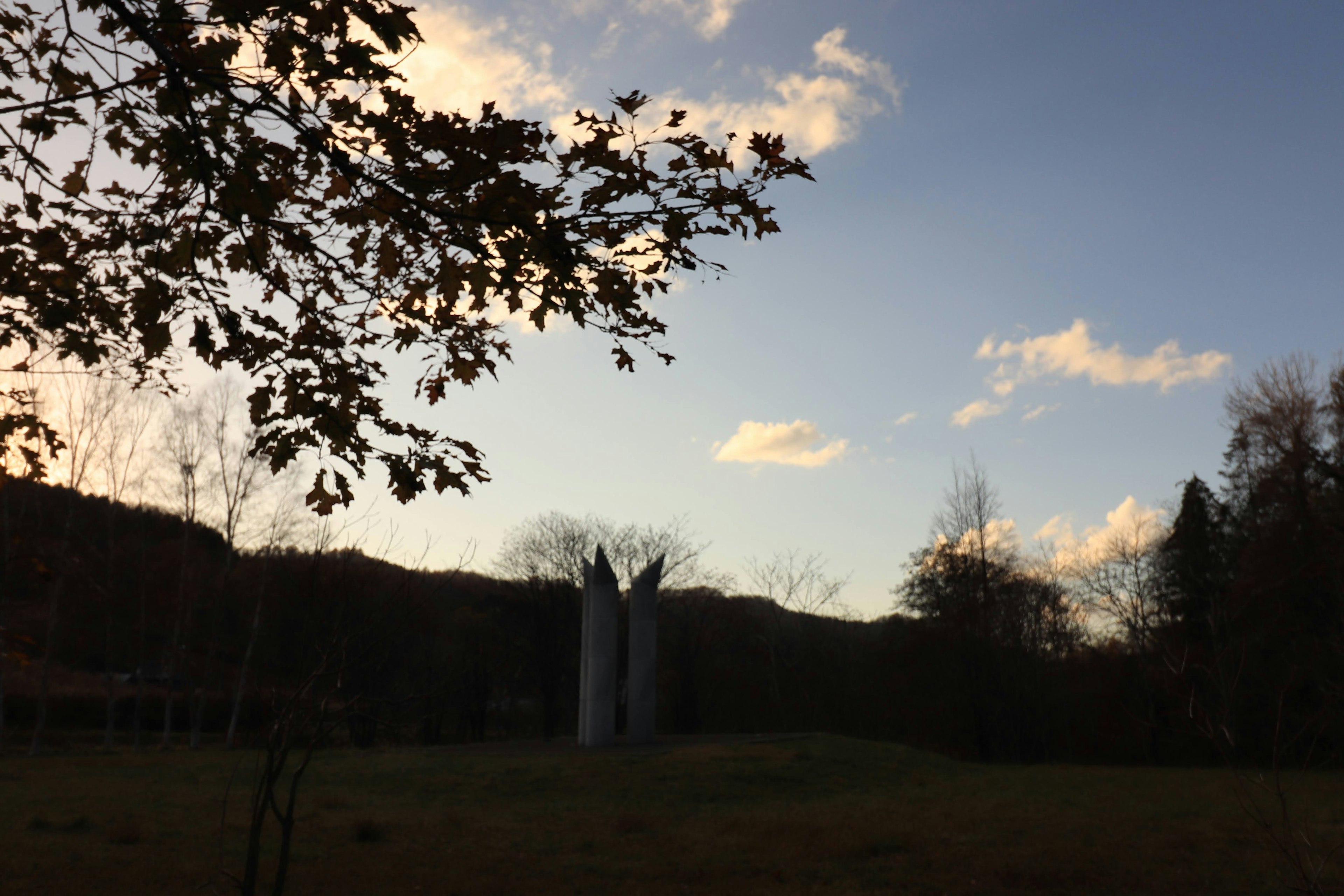 夕暮れ時の風景に立つ彫刻的な構造物と木々