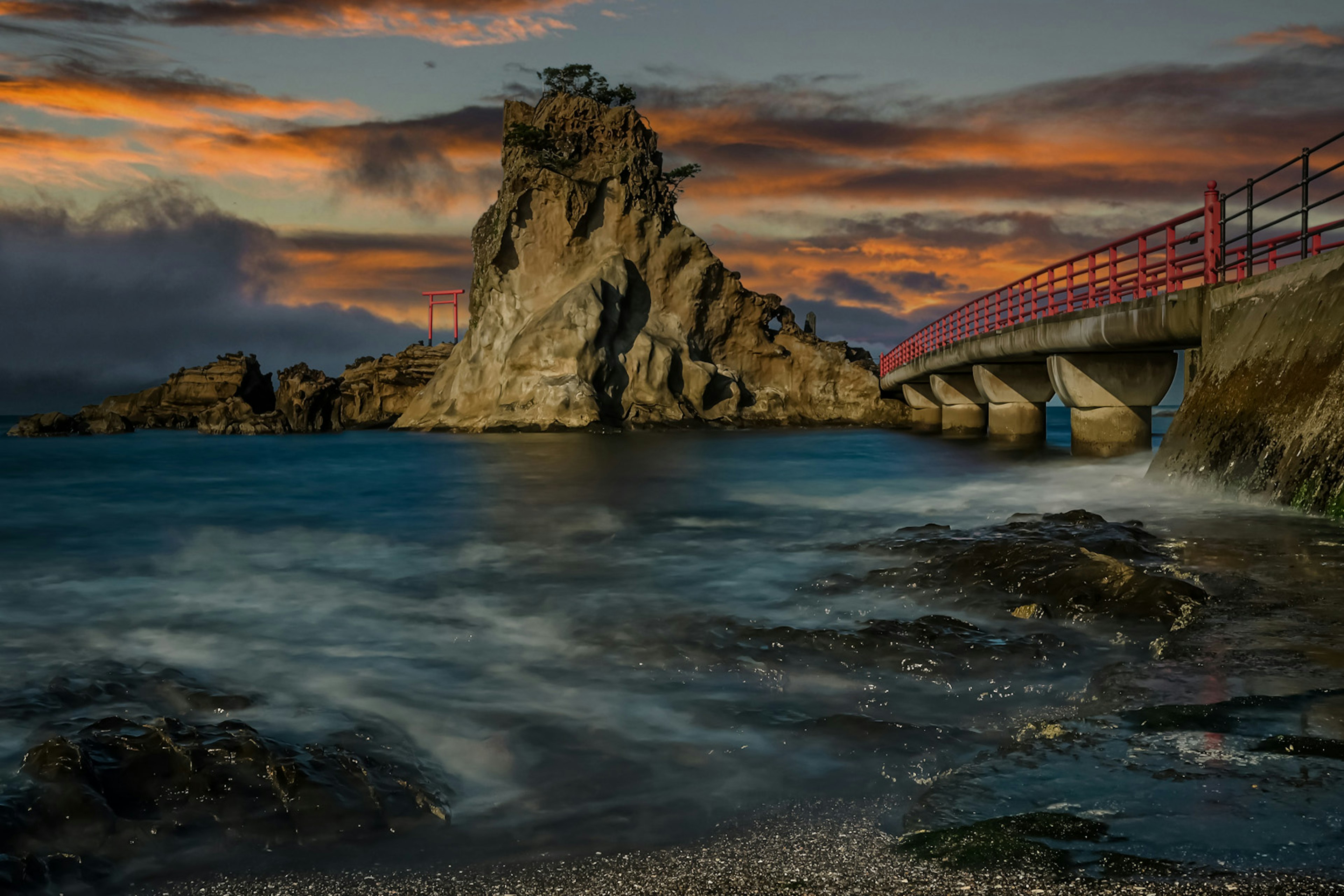 Scenic view of a rocky island with a red bridge at sunset