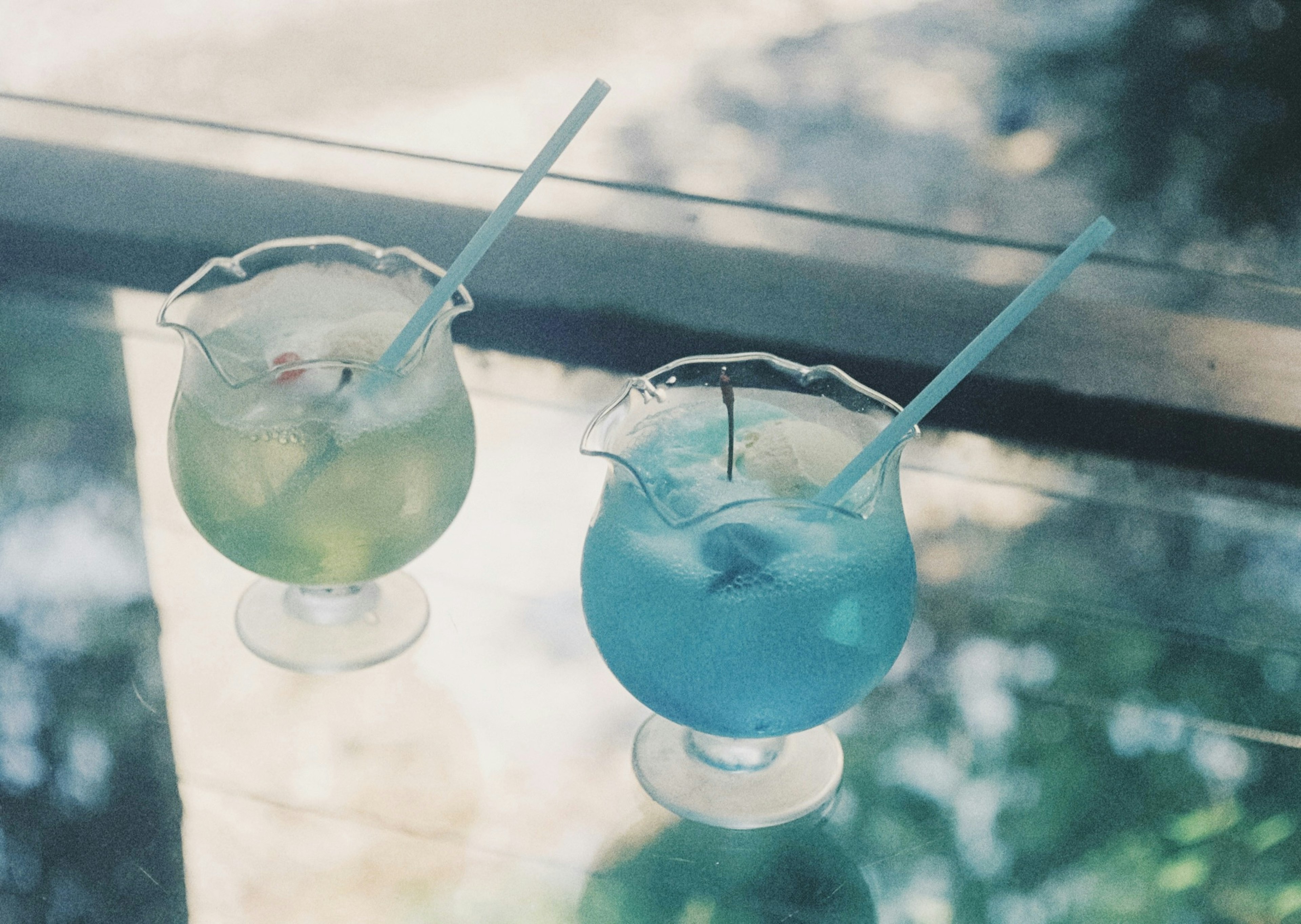 Two cocktails in green and blue on a glass table