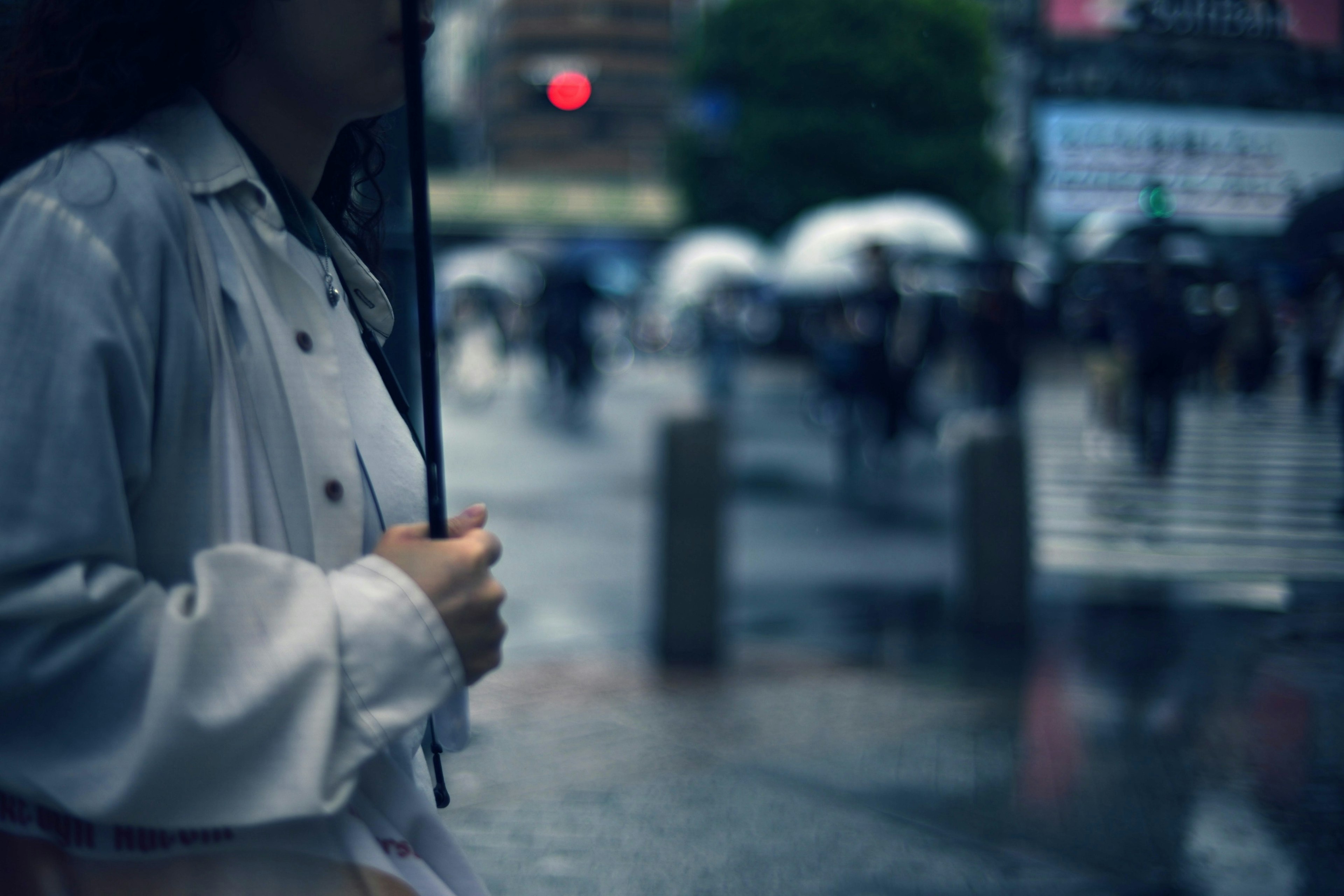 Frau mit einem Regenschirm im Regen und unscharfen Passanten im Hintergrund