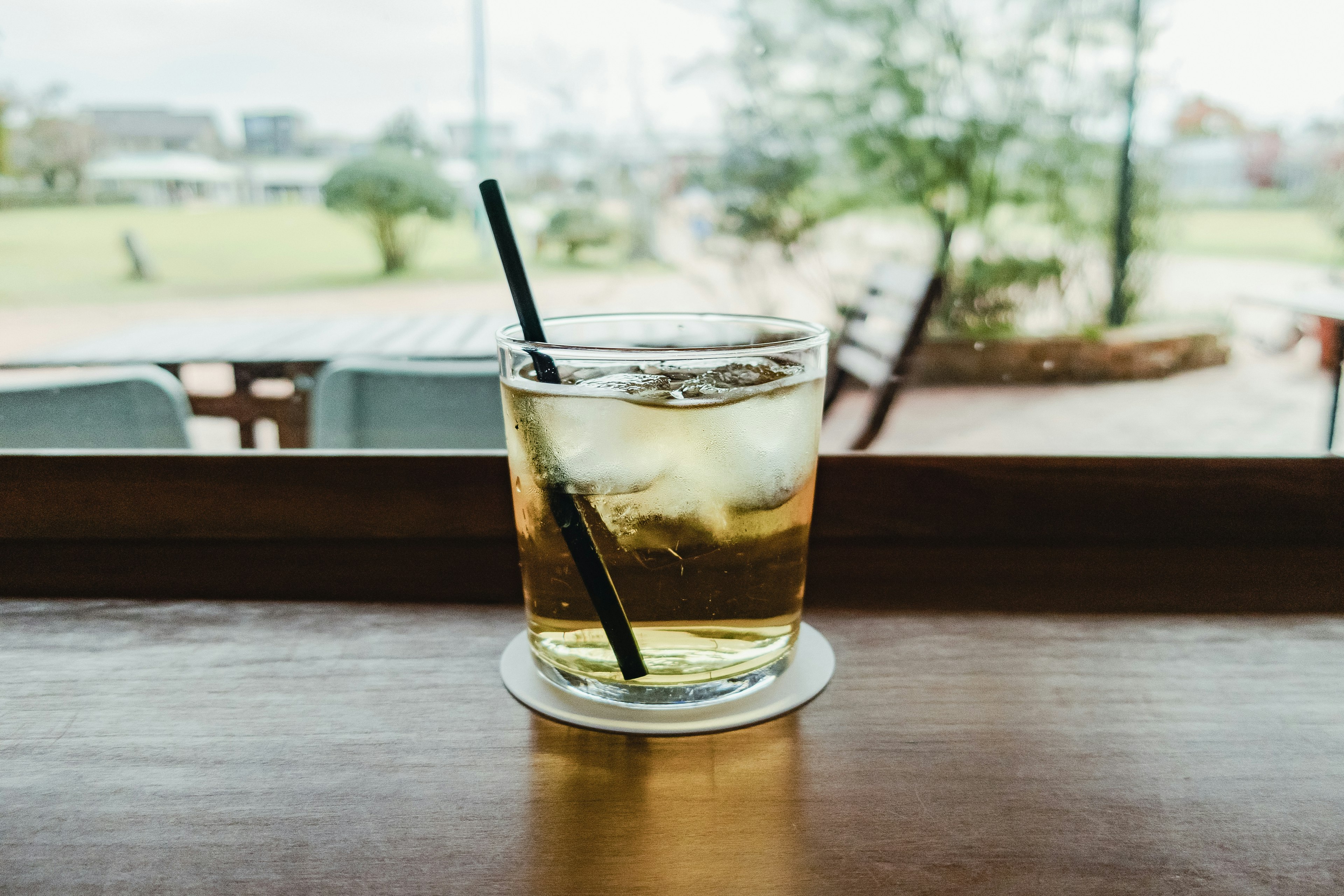 A glass of iced drink on a wooden table with a green outdoor view in the background