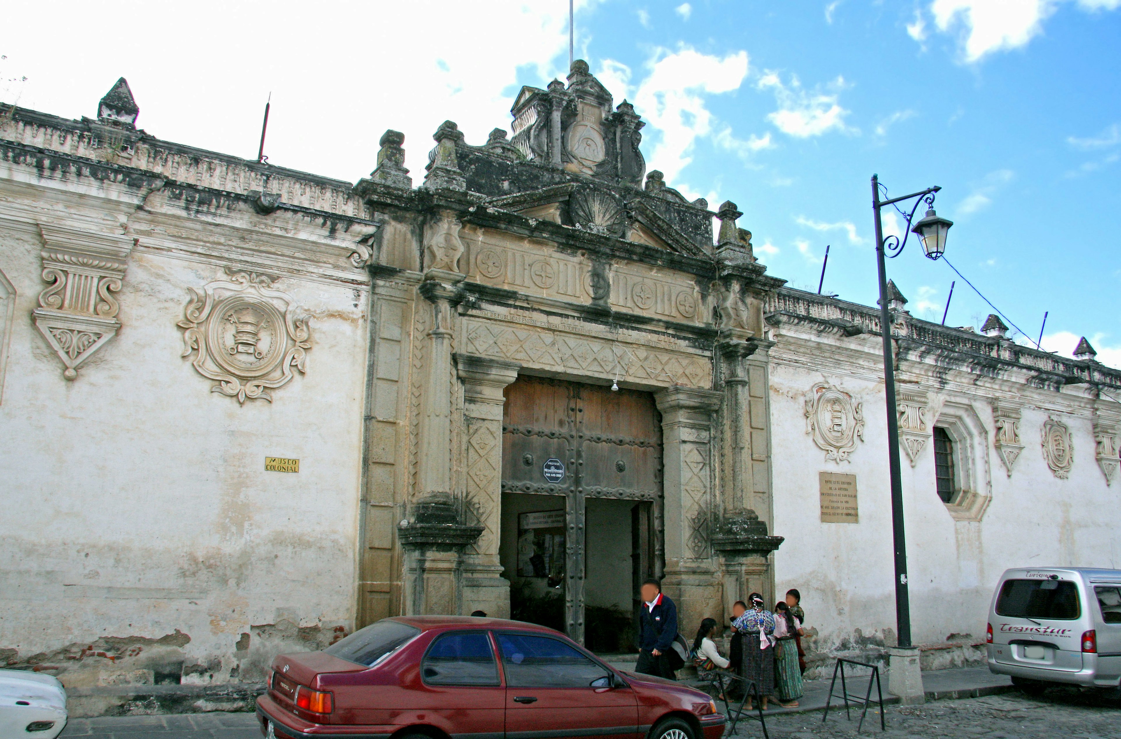 Façade d'un vieux bâtiment avec des sculptures détaillées une voiture rouge et des gens à proximité