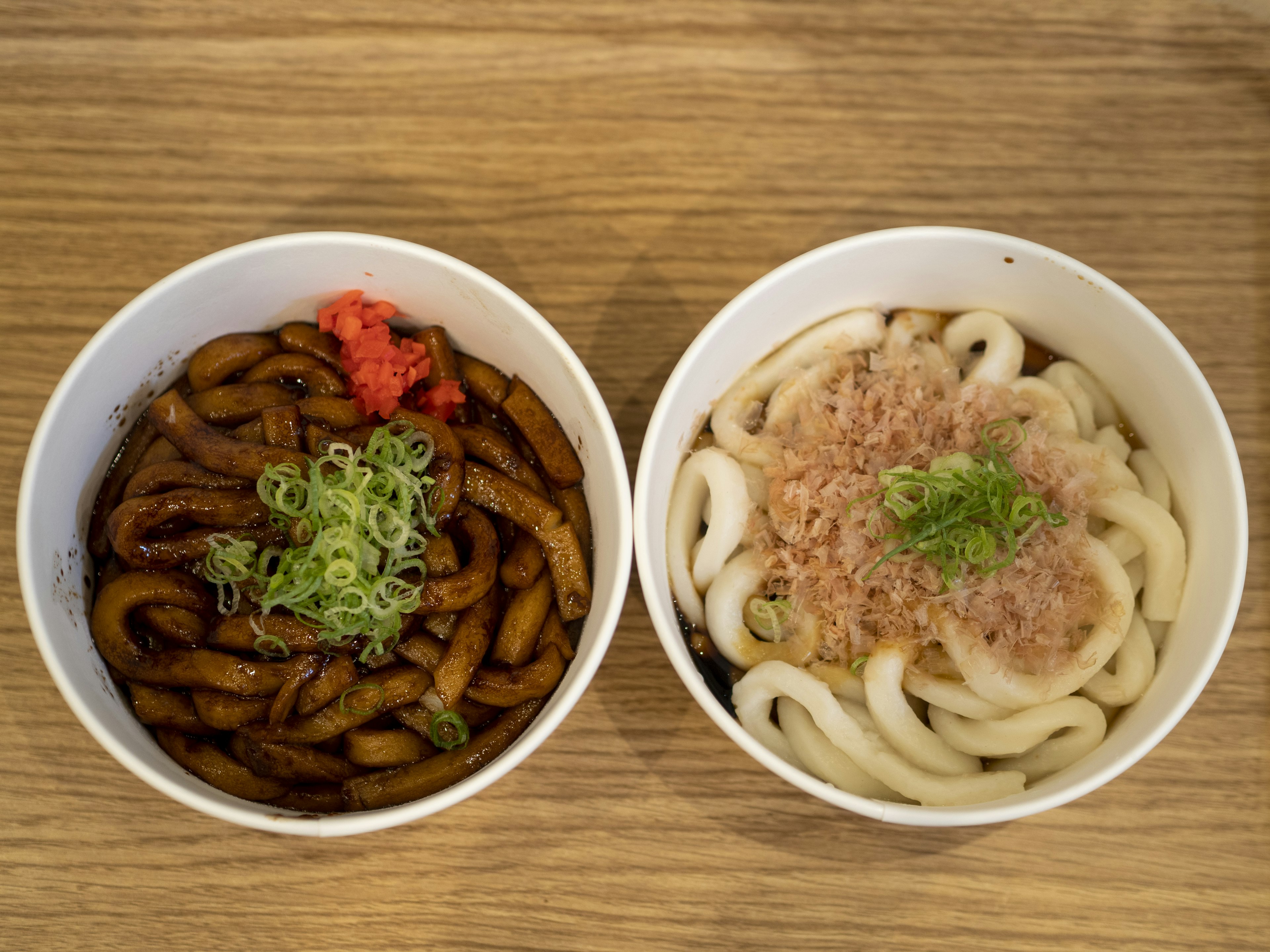 Dua mangkuk hidangan udon Satu mangkuk memiliki udon dengan saus gelap dihiasi dengan bawang hijau dan jahe acar Mangkuk lainnya berisi udon putih yang dihiasi dengan serpihan bonito dan bawang hijau