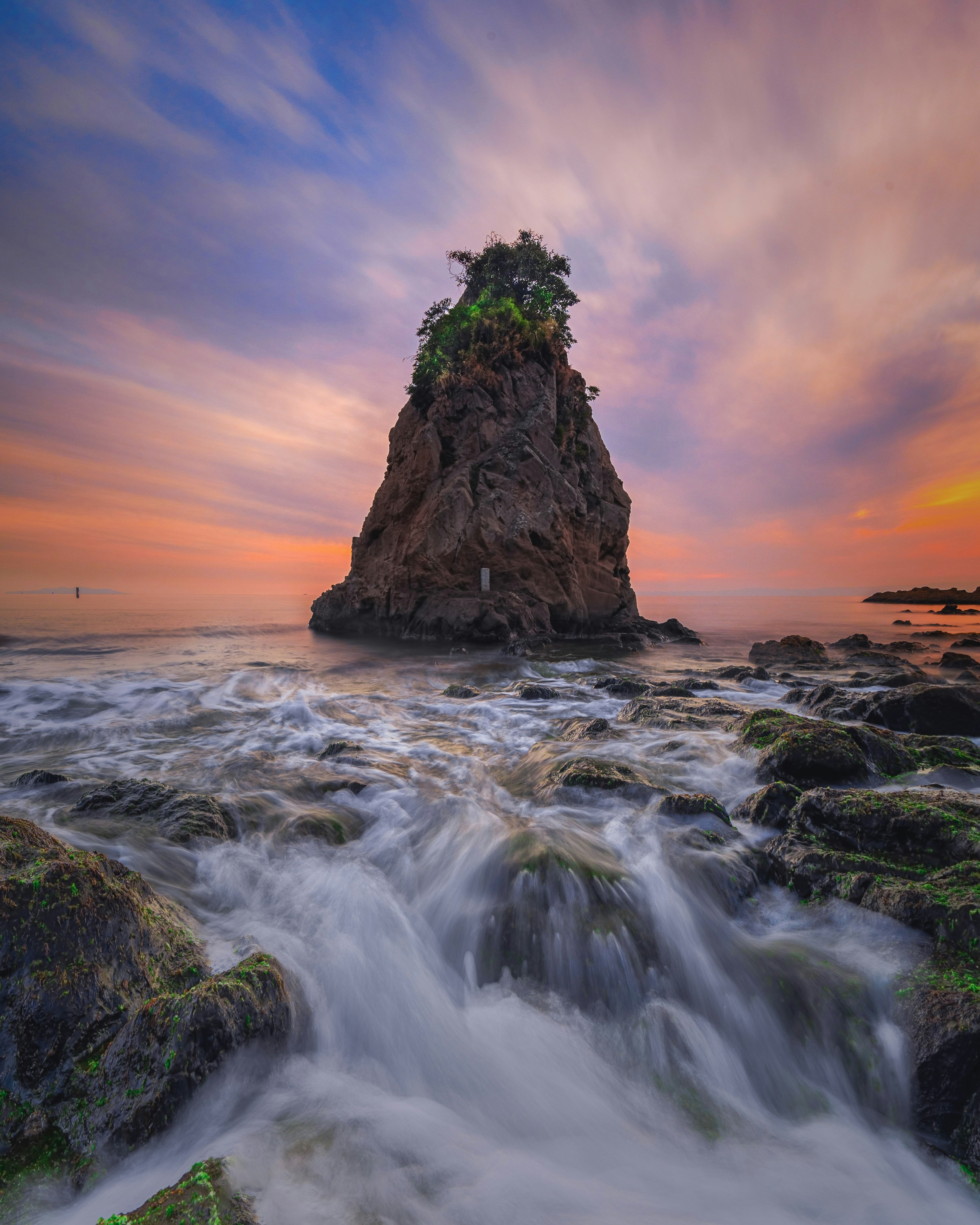 Una formazione rocciosa con vegetazione sopra sotto un cielo colorato al tramonto sull'oceano