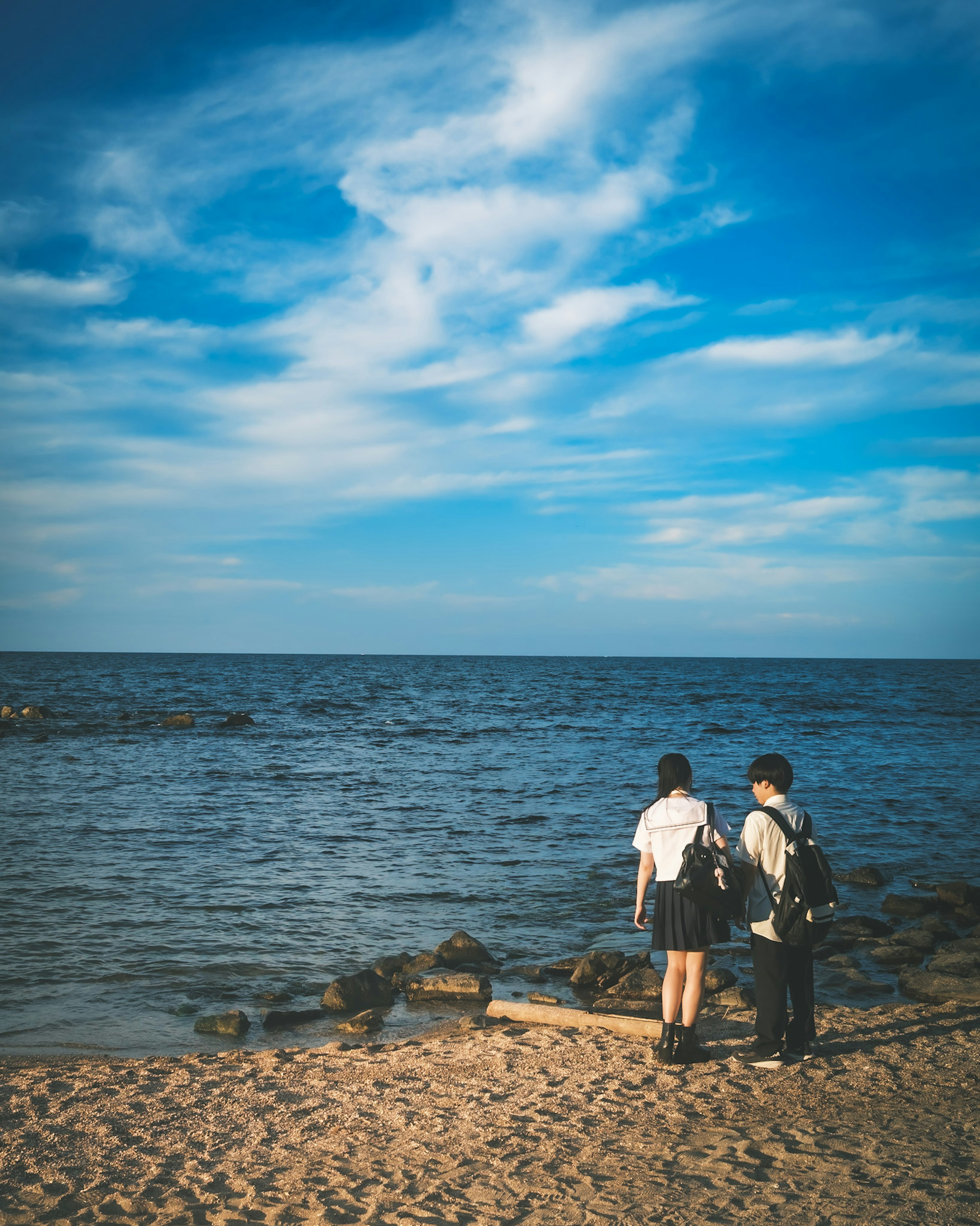 Dua siswa berbicara di pantai dengan langit biru dan laut tenang