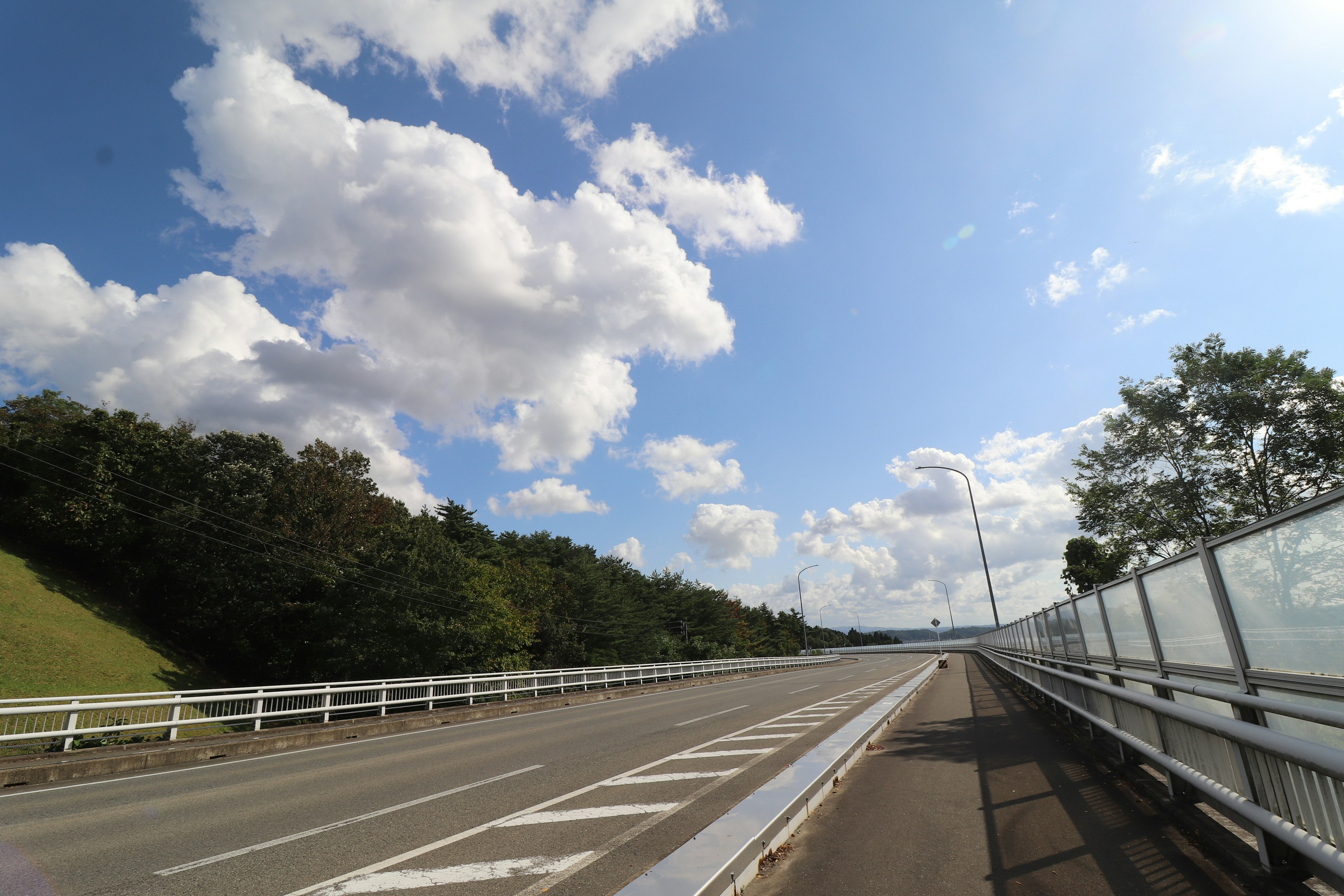 Une route bordée de verdure sous un ciel bleu avec des nuages blancs duveteux