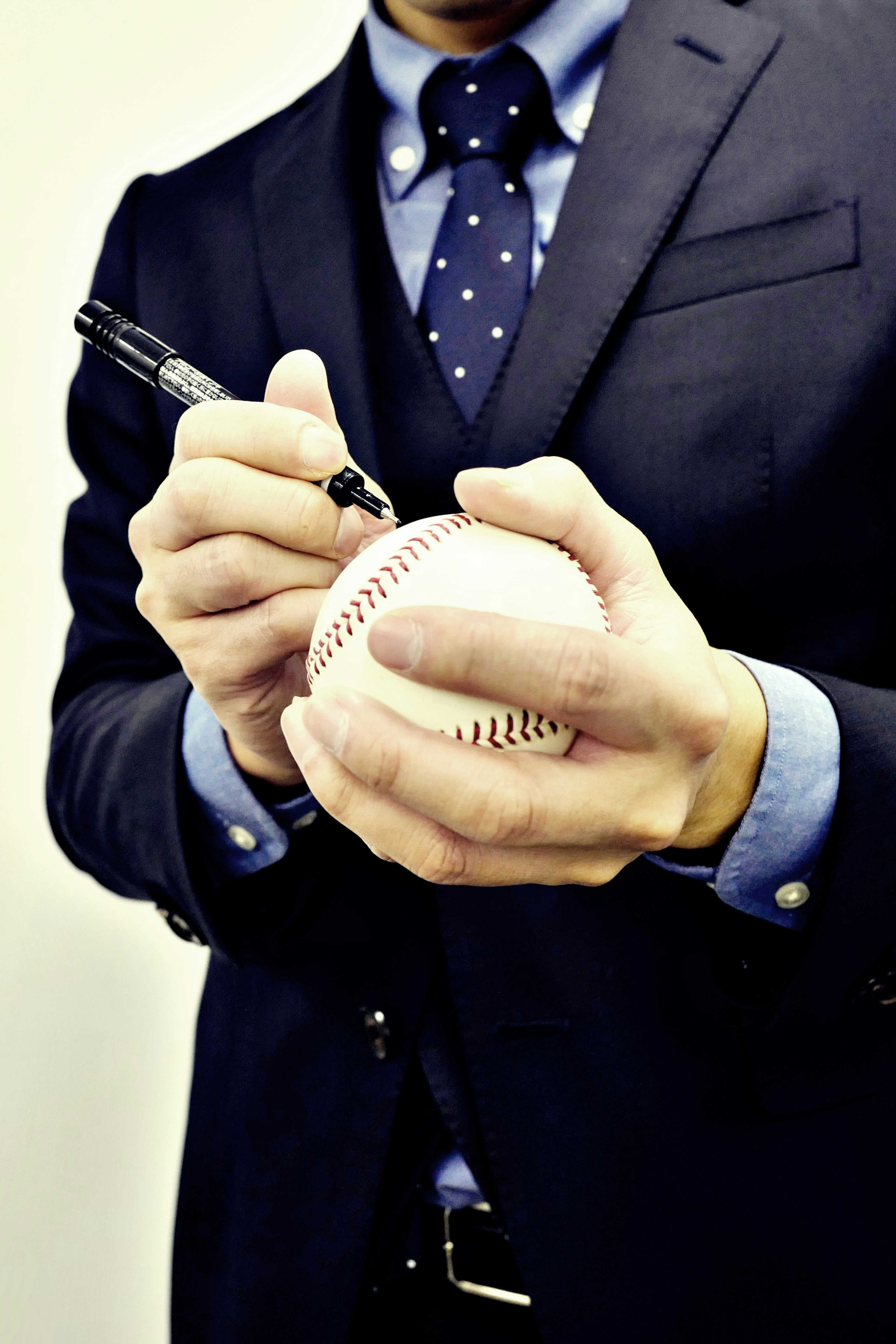 A man in a suit signing a baseball