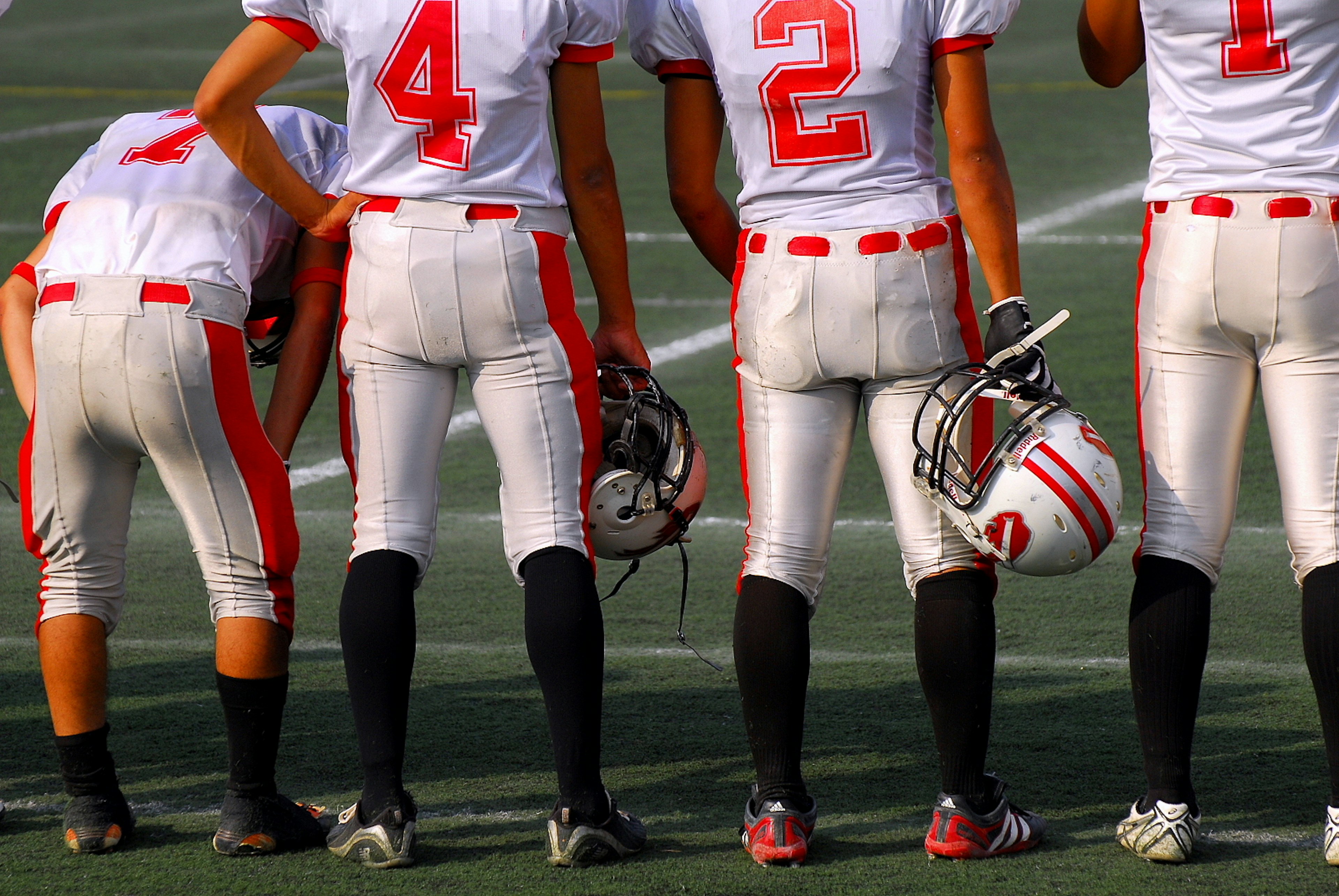 Football players standing on the field wearing white and red uniforms holding helmets