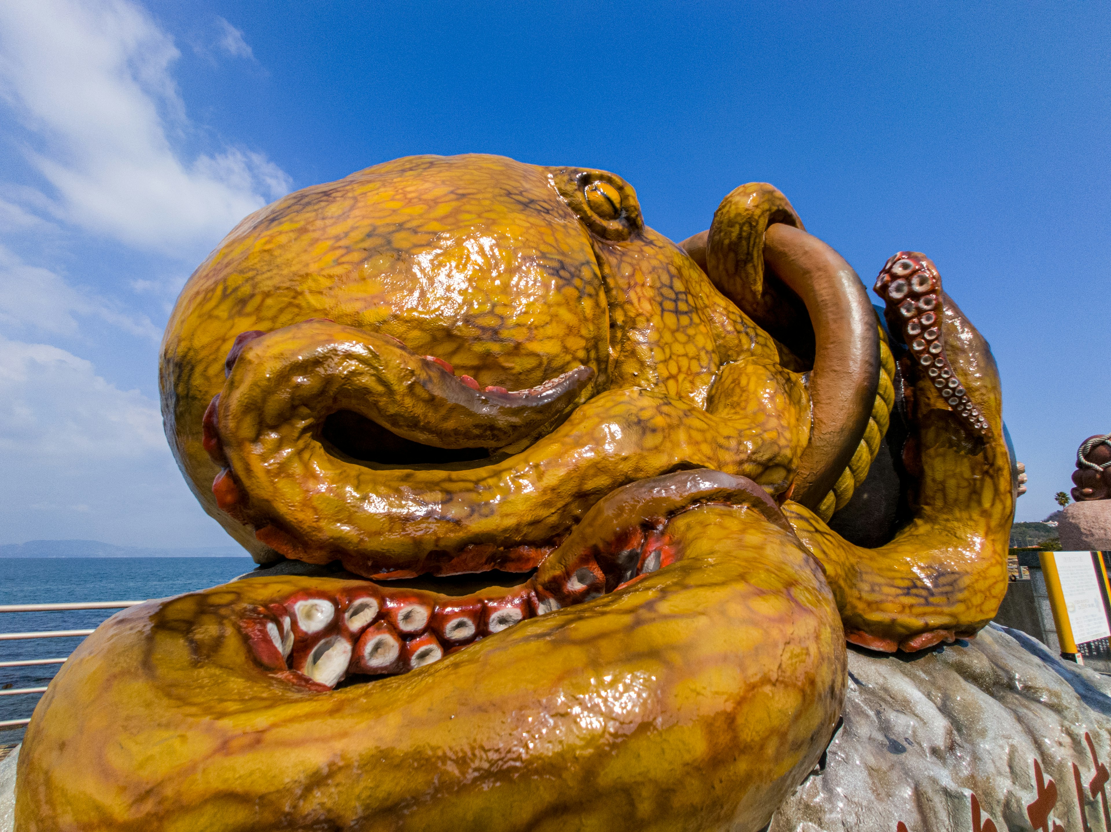 Patung gurita kuning besar di latar belakang laut