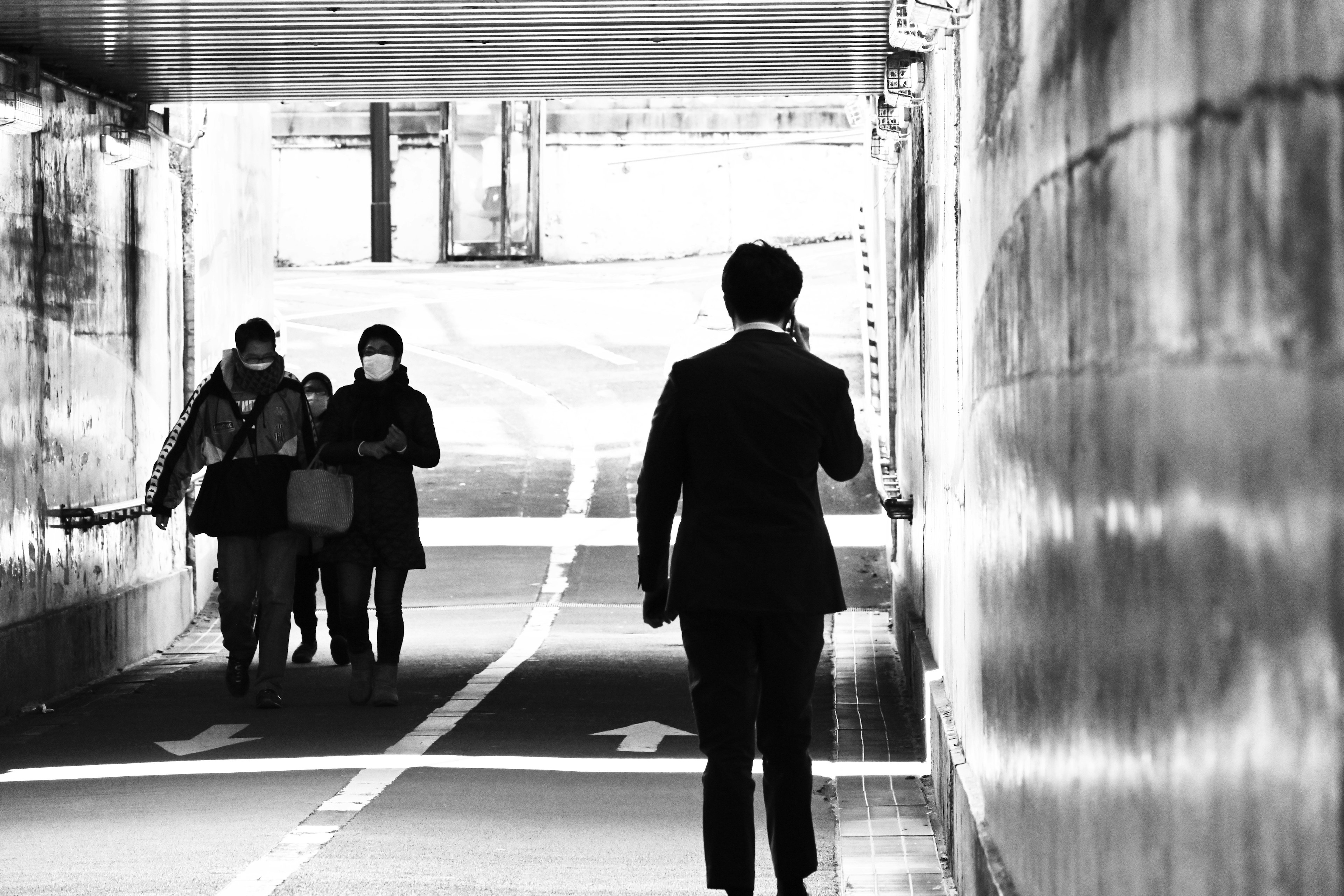 Un hombre de negocios caminando en un túnel con peatones enmascarados