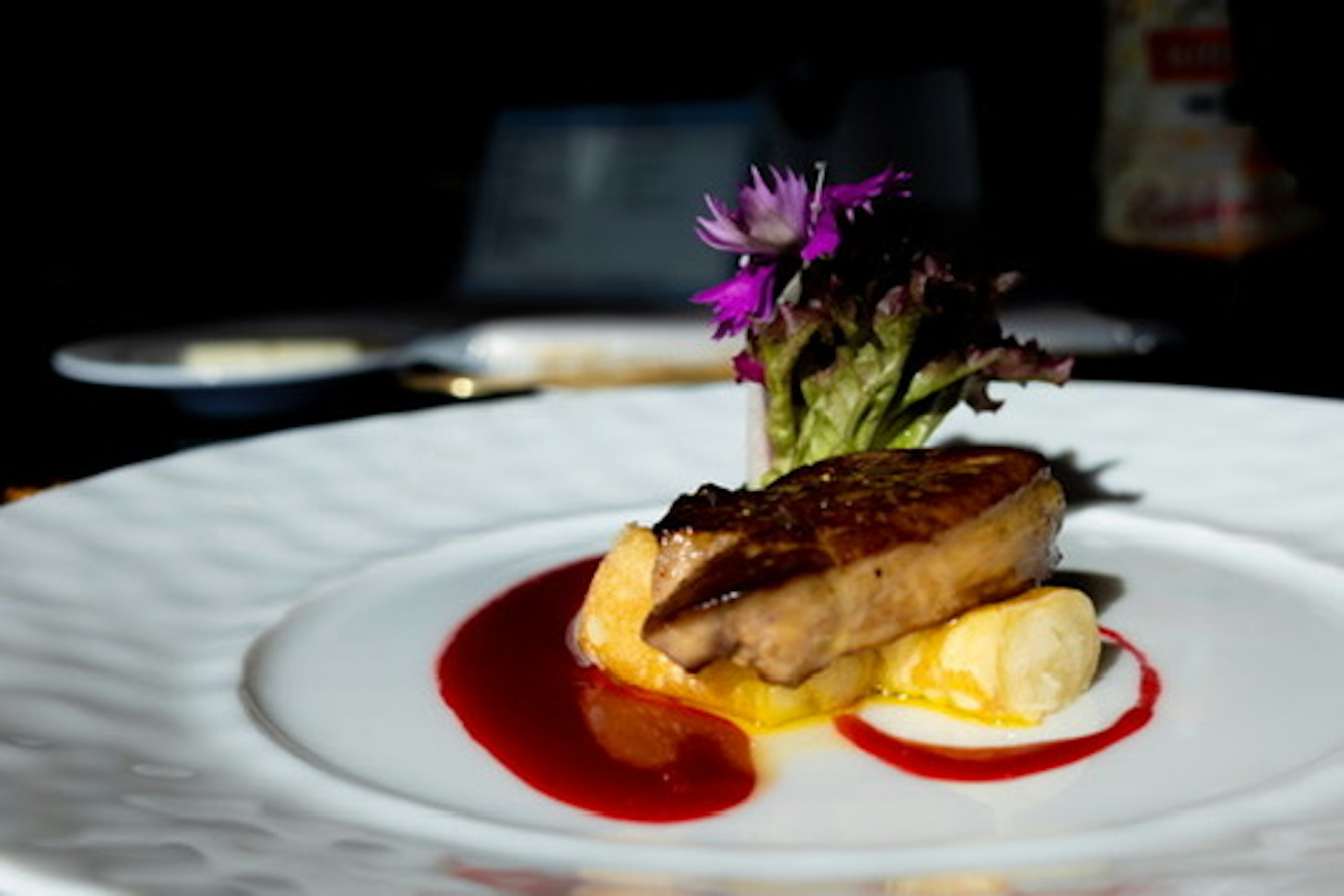 Un plato de pato bellamente presentado con salsa de fruta y decorado con flores