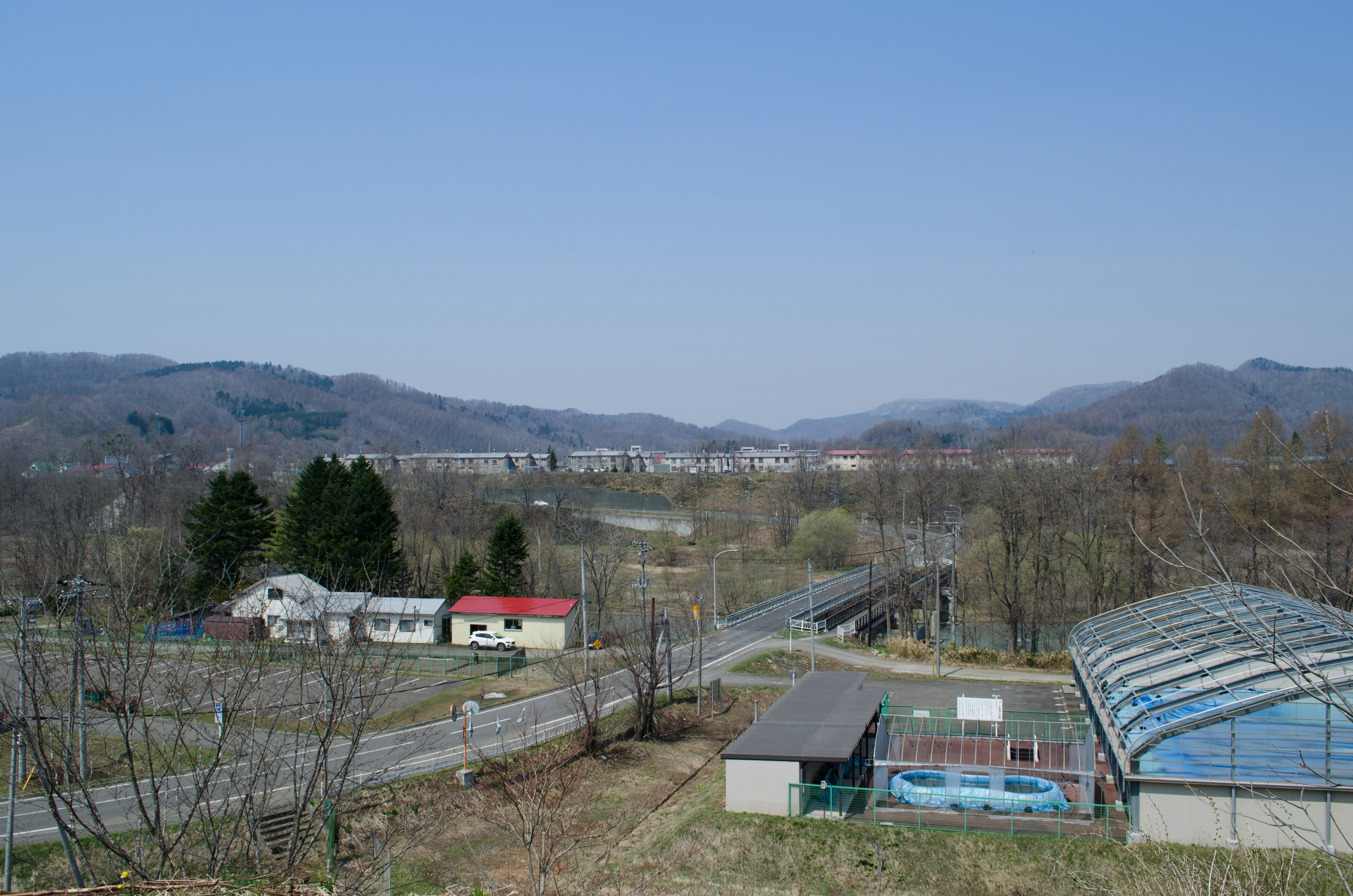 Landschaft unter blauem Himmel mit Häusern und einem Gewächshaus und grünen Bergen im Hintergrund