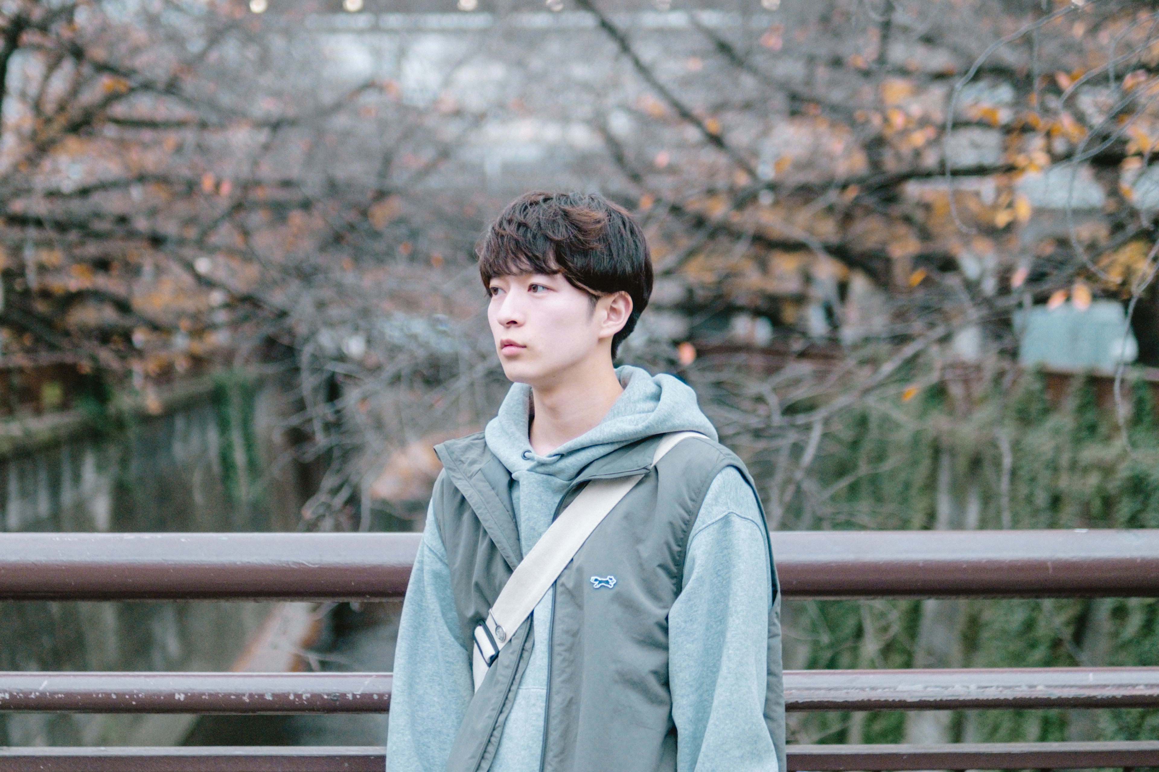 Young man standing on a park bridge with winter trees in the background