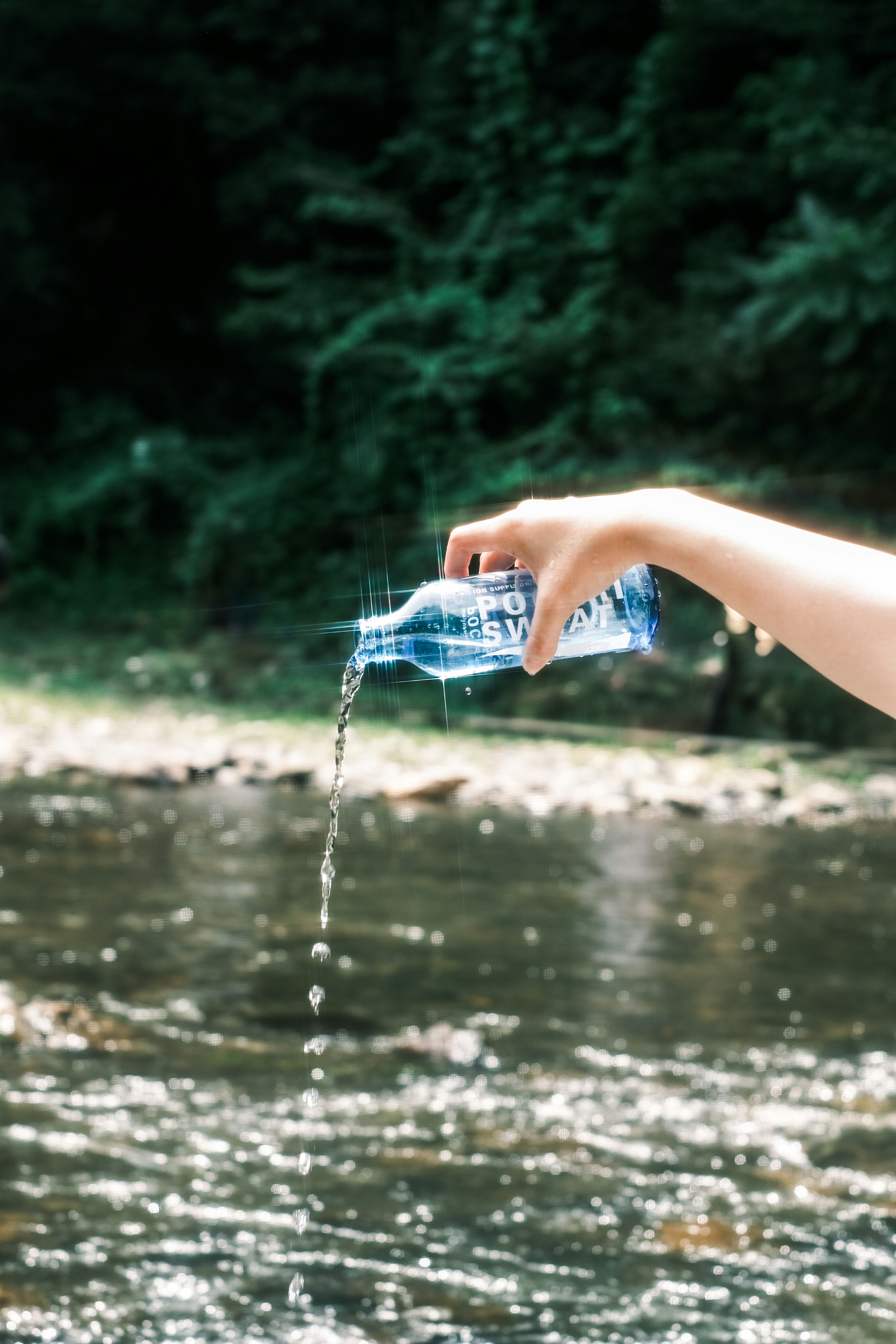 Mano che versa acqua da una bottiglia blu in un fiume