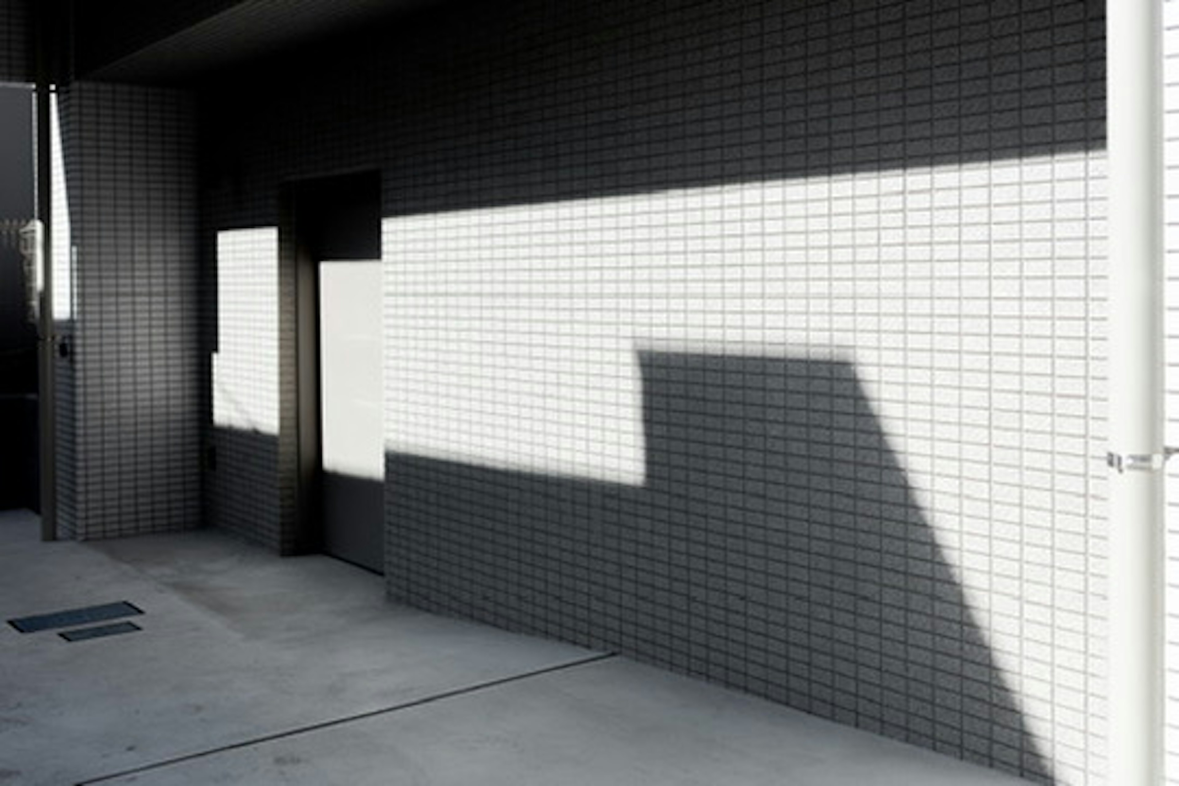 Extérieur d'un bâtiment avec un mur de carreaux blancs et des ombres marquées