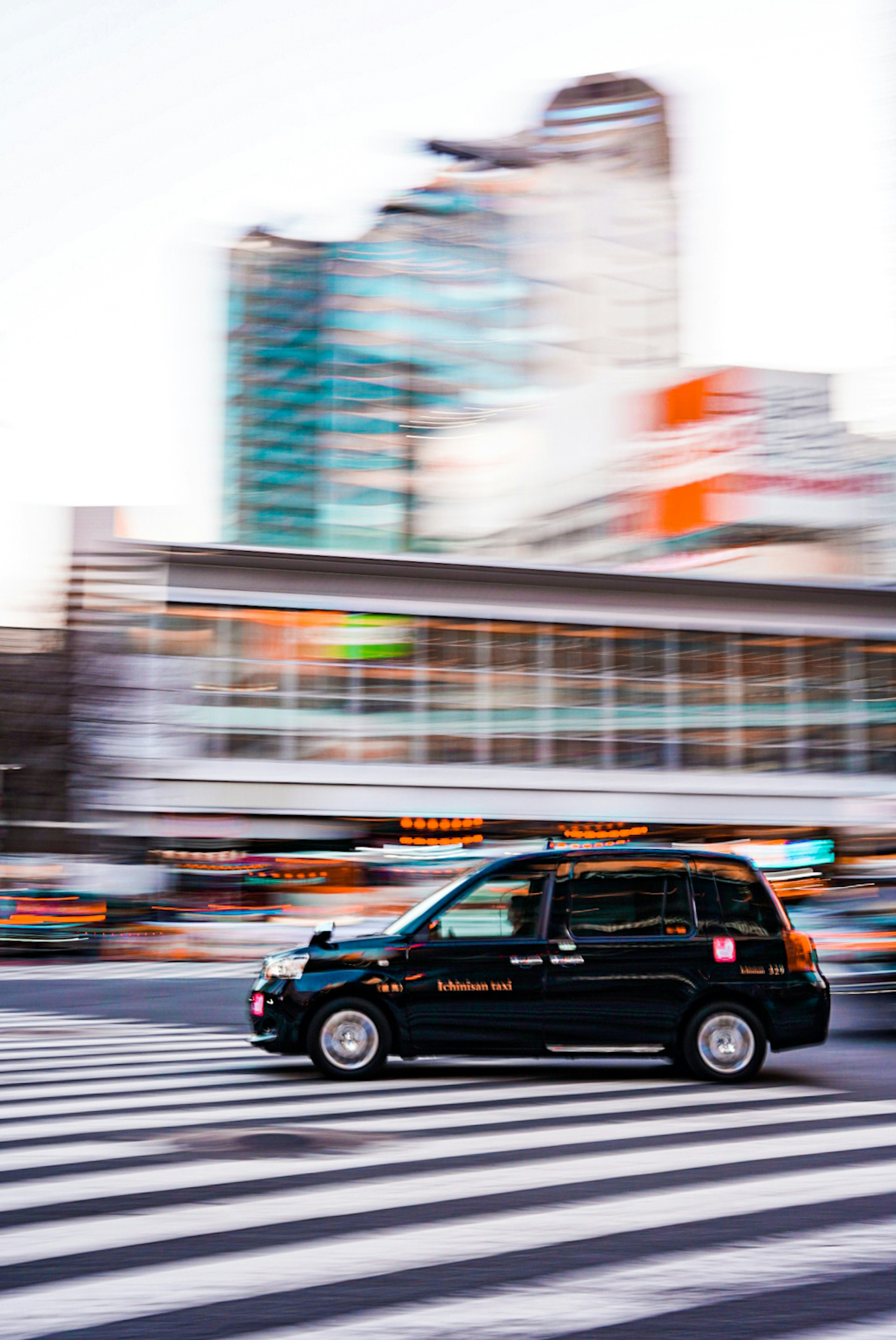 A black taxi speeding through a crosswalk with a blurred city background