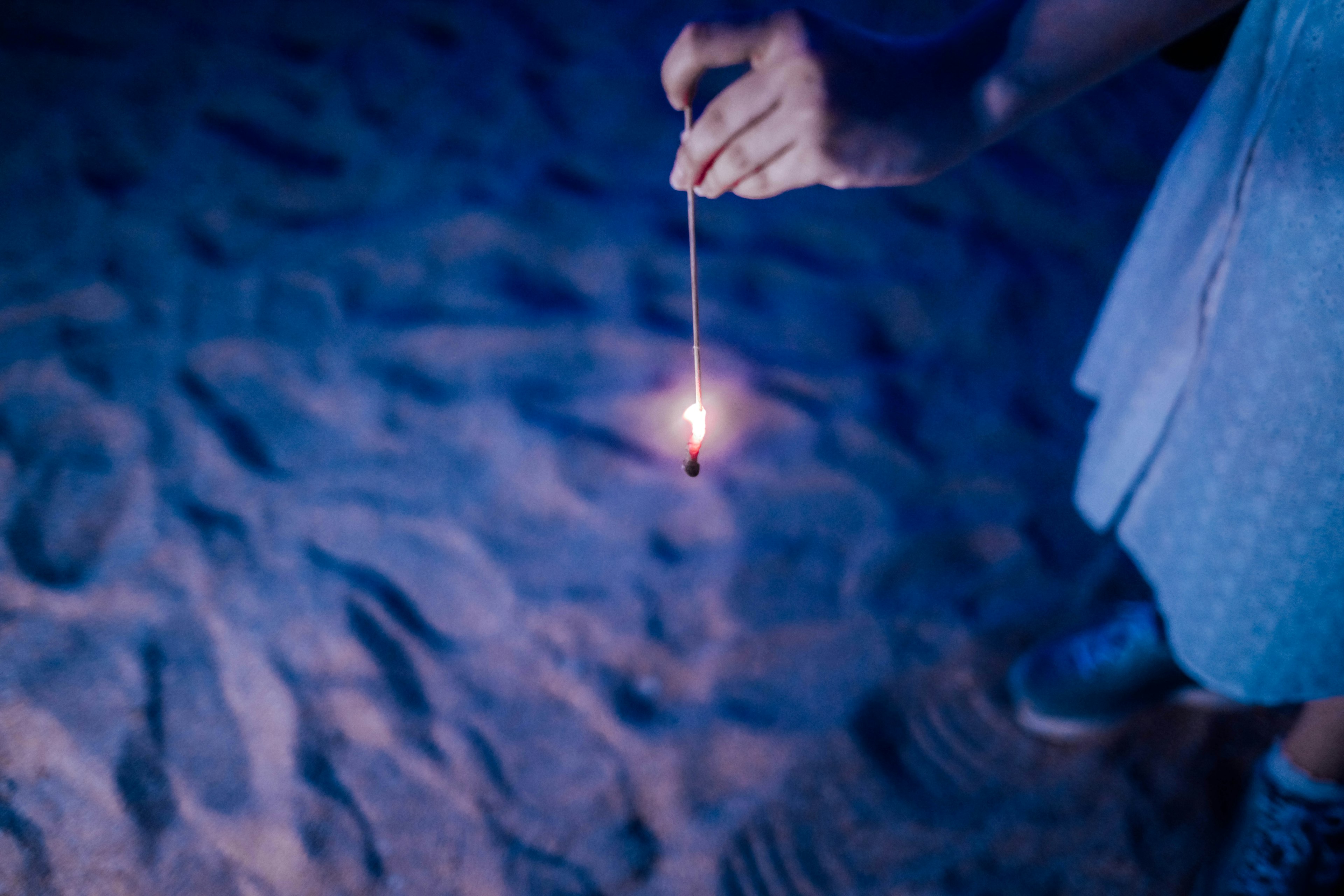 Close-up of a hand holding a sparkler on the beach in a blue light with the spark flickering