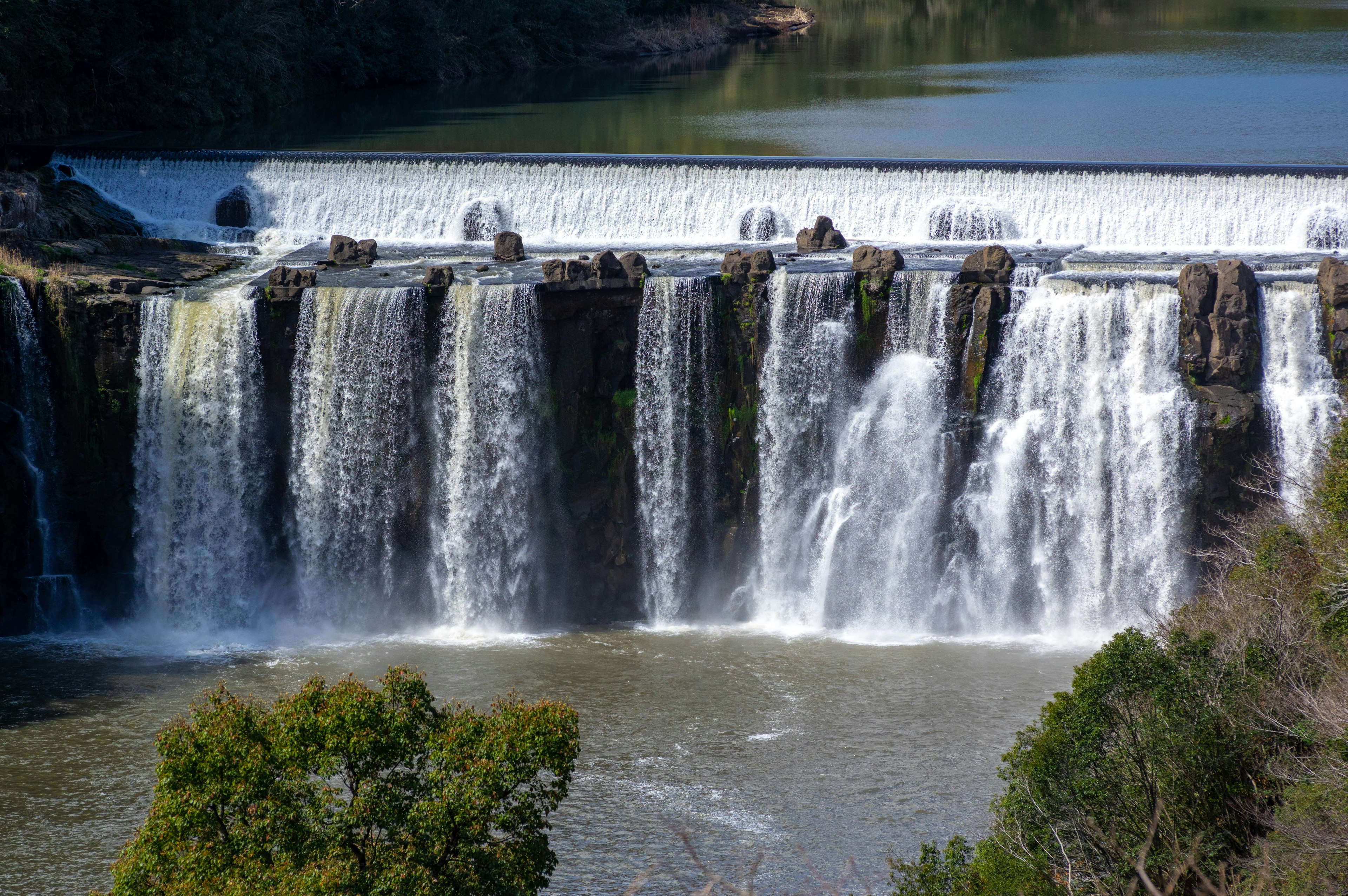 Vista panoramica di una cascata con acqua che scorre e vegetazione rigogliosa sotto un cielo blu